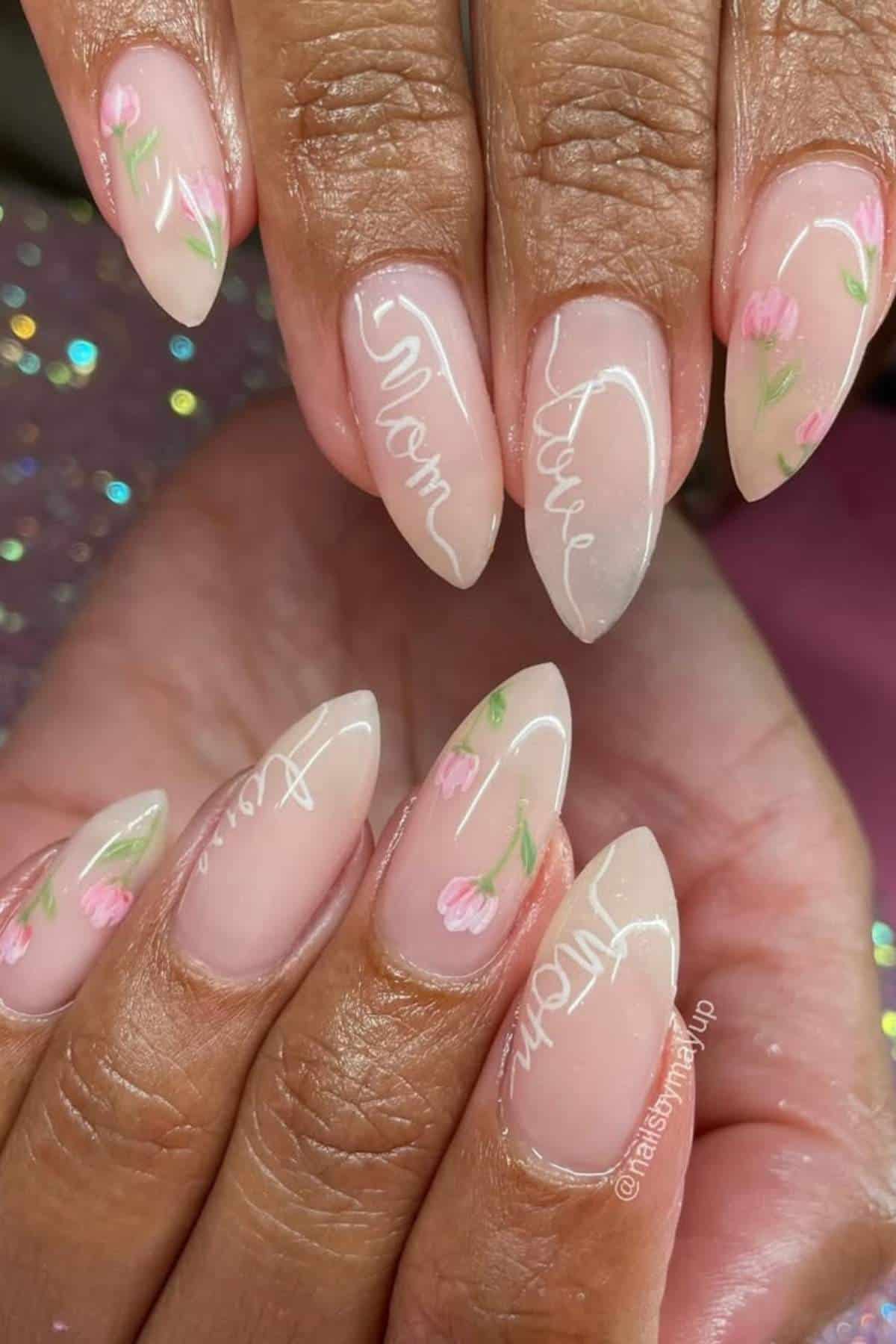 Hands with almond-shaped nails featuring a light pink base, small painted tulips, and white cursive text reading "Mom, You're Wow.