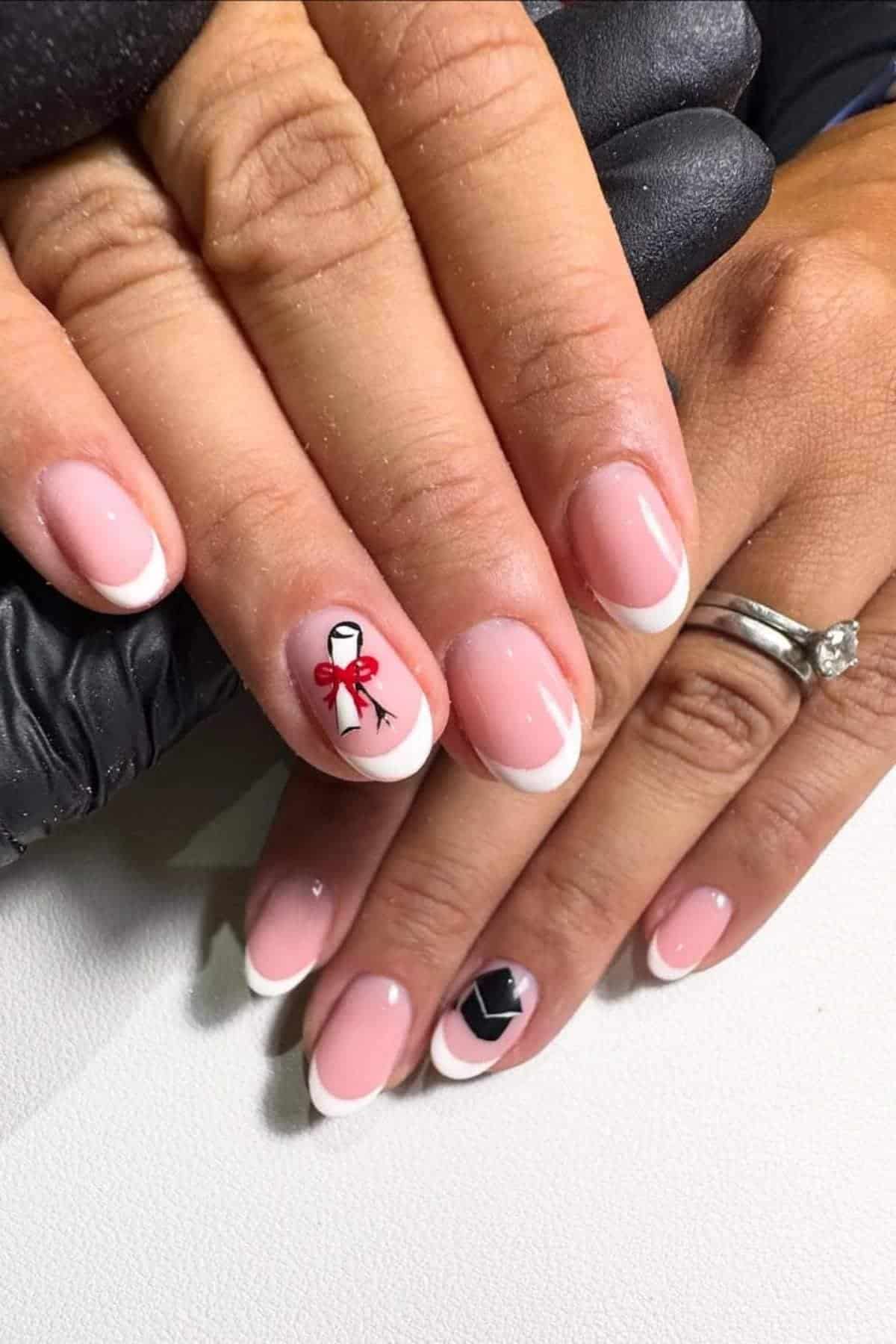 Hands with French manicure; one nail has a painted red bow and diploma, another features a black graduation cap design.