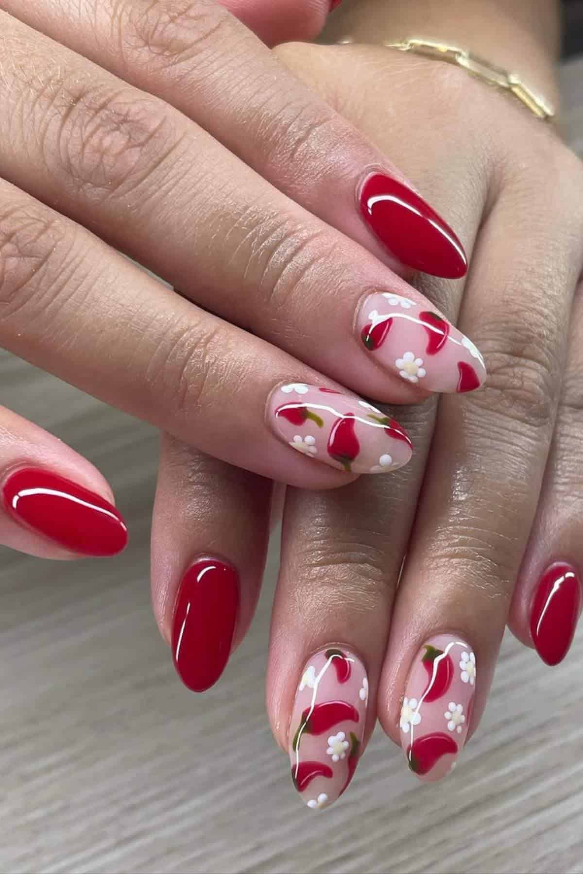 Hands with almond-shaped nails; some nails are painted glossy red, others have a clear base with red cherries and small white flower designs.