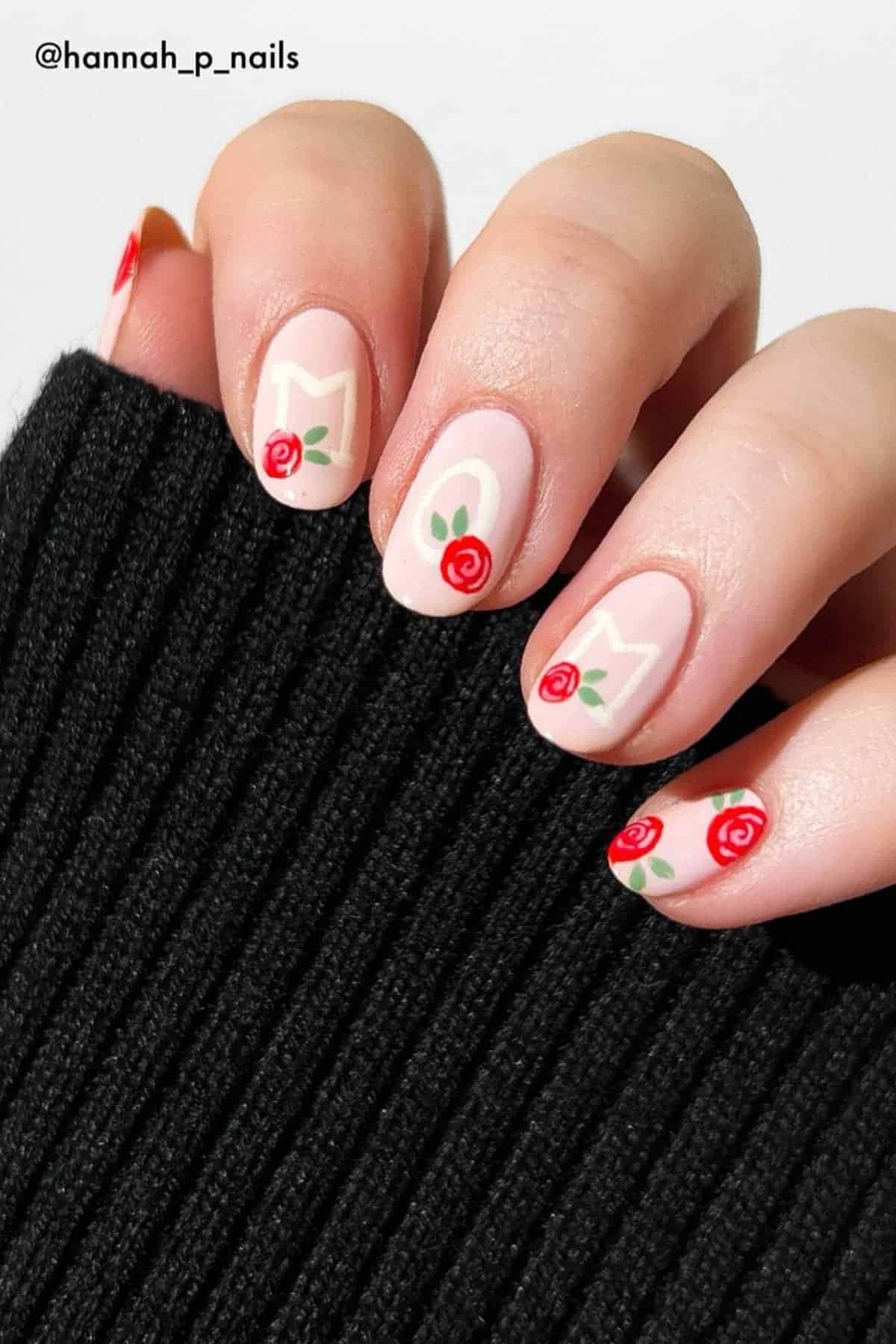 A hand with pale pink nails displays the word "MOM" in white letters and red rose designs on each nail. The person is wearing a black ribbed sweater.