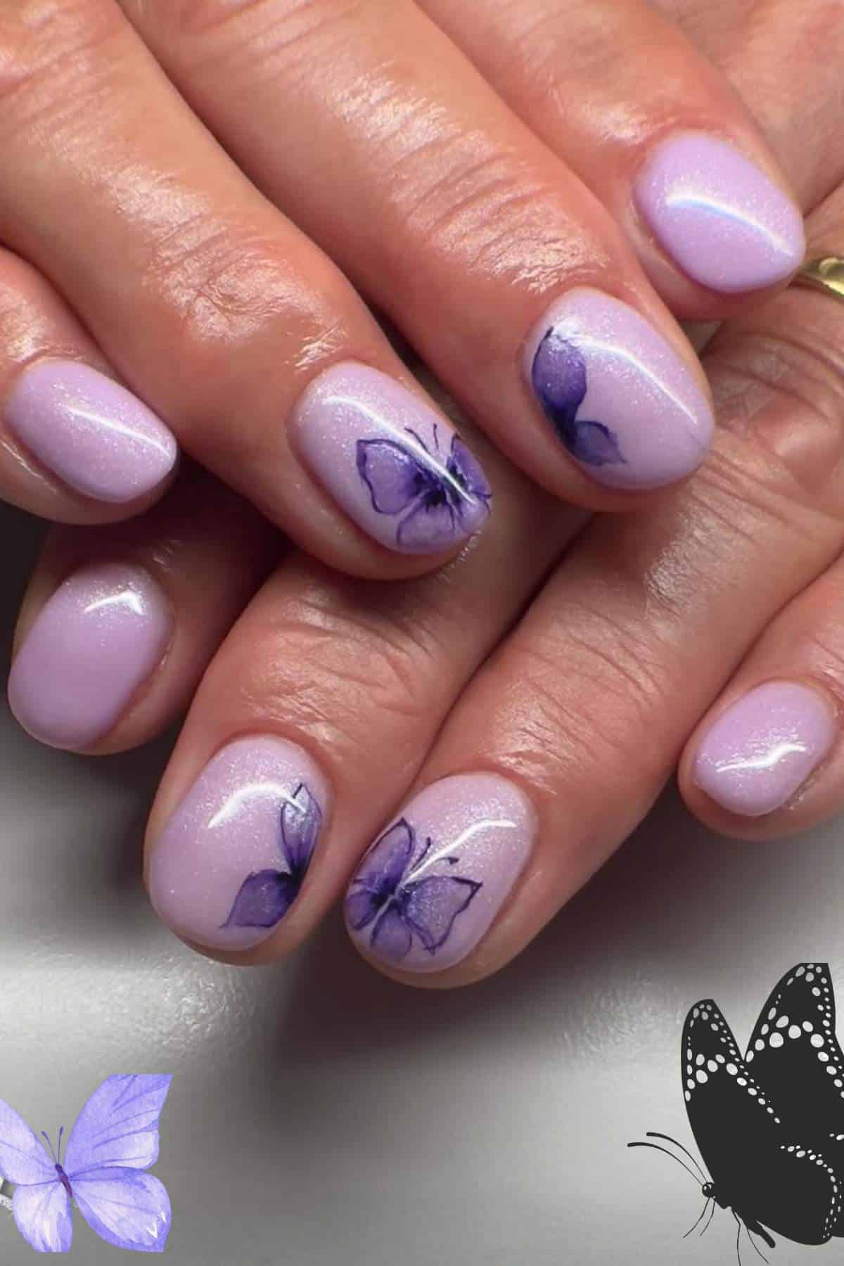 Close-up of hands with short, light purple nails featuring butterfly designs on a few nails; hands are gently resting on each other.