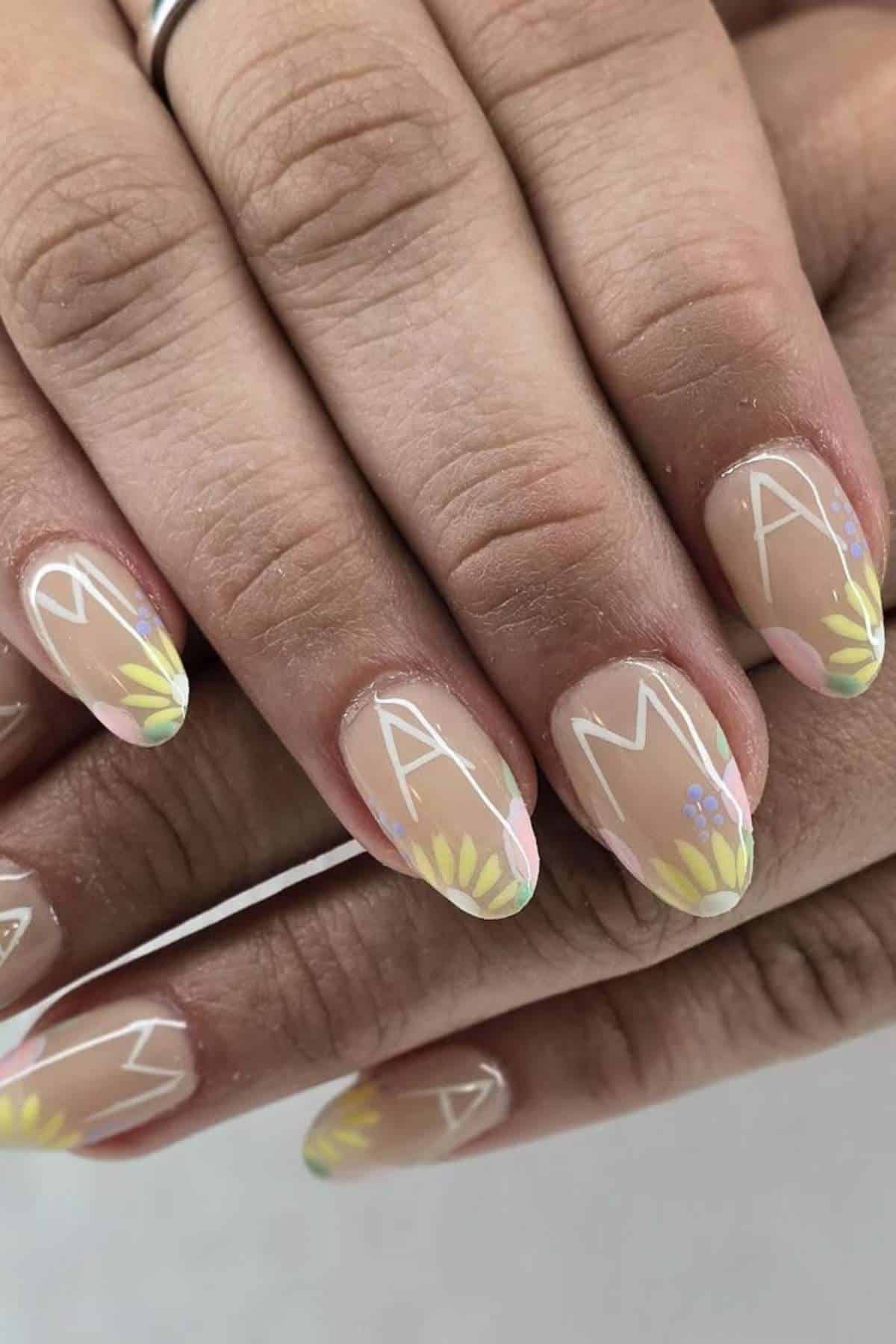 Close-up of hands with nails painted in a floral design and each nail featuring a white letter, collectively spelling "MAMA.