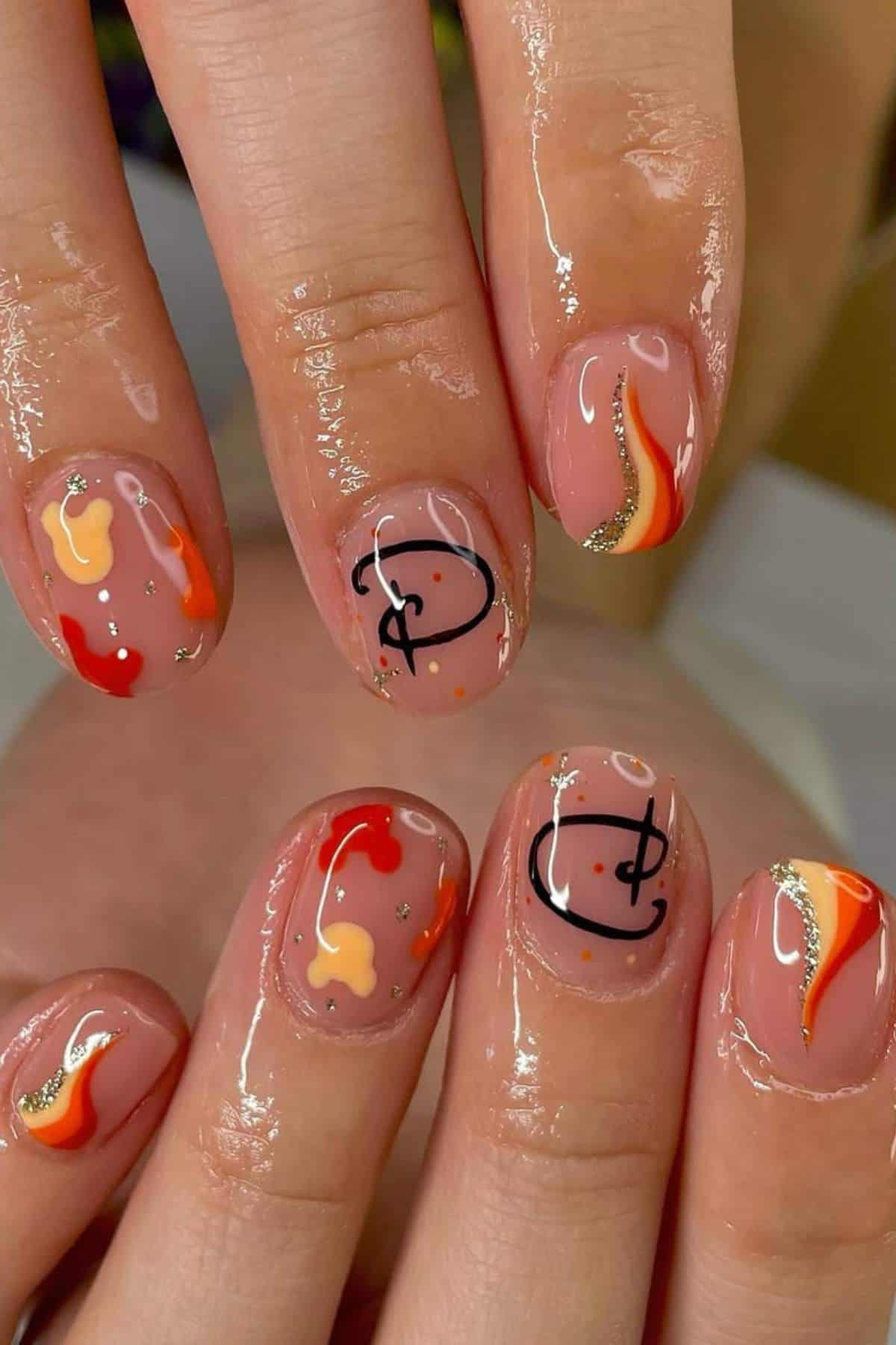 Close-up of glossy manicured nails with abstract orange, yellow, and gold designs, along with black outlined symbols on a nude base.