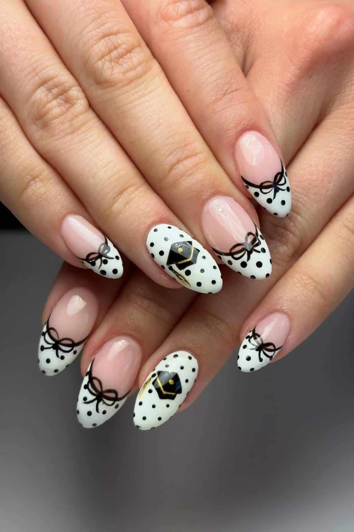 Close-up of hands with almond-shaped nails featuring a black bow and polka dot design on a white background, with accent nails showing a black envelope motif.