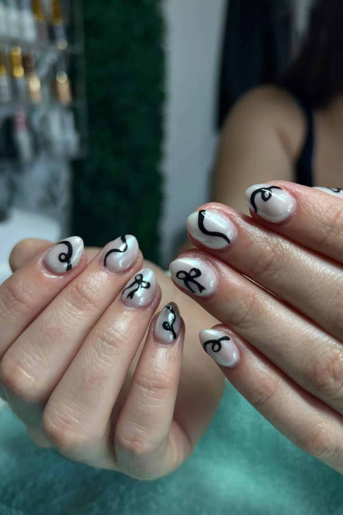 Close-up of hands with almond-shaped nails painted in a light base color and decorated with black abstract line art designs.