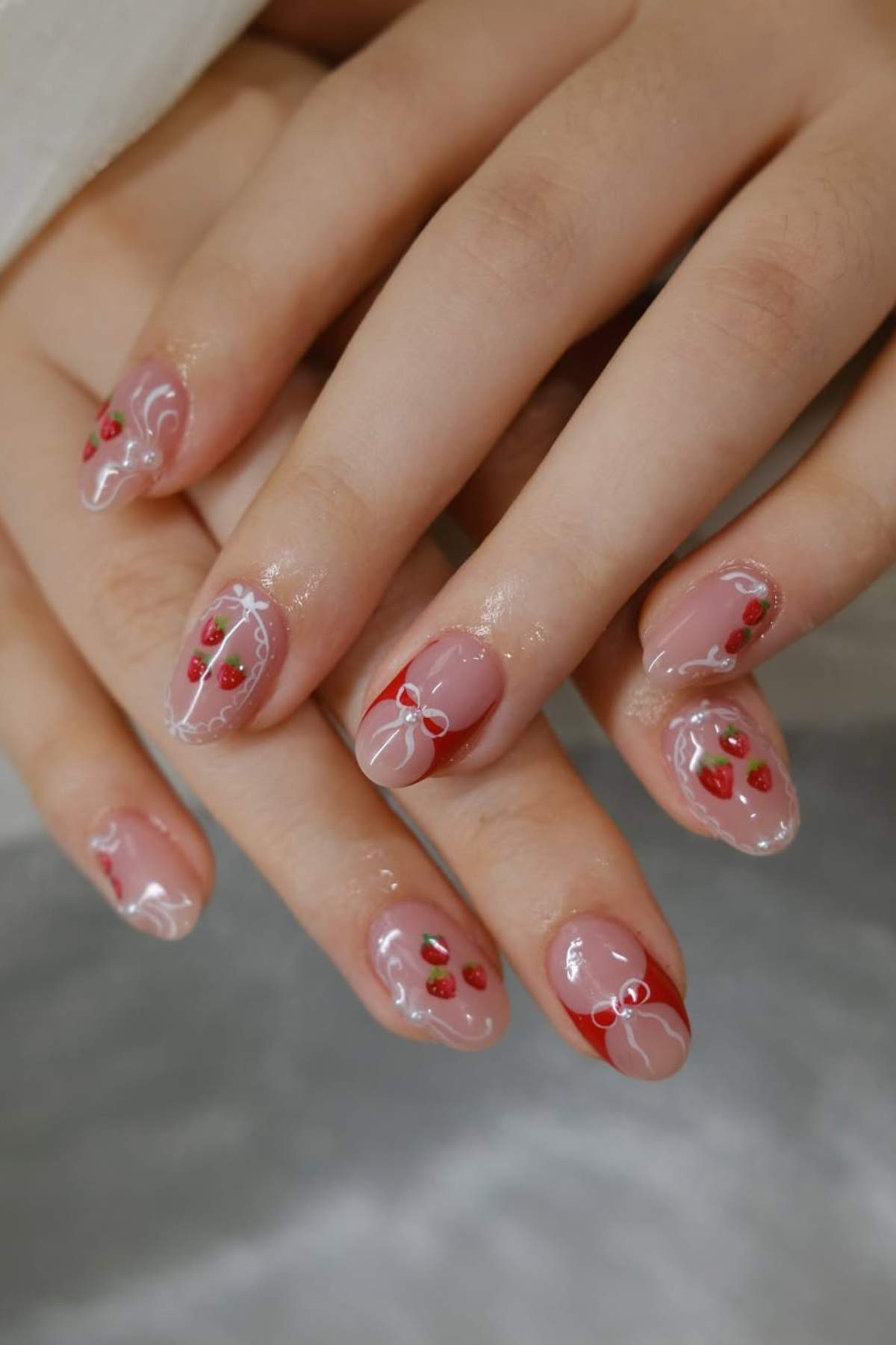 Close-up of hands with manicured nails featuring small strawberry designs and white line accents on a nude pink base.