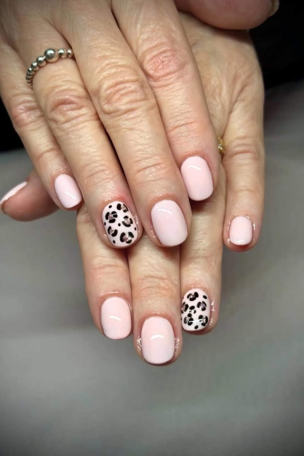 Hands with short, light pink manicured nails; ring fingers feature black and white leopard print nail art.