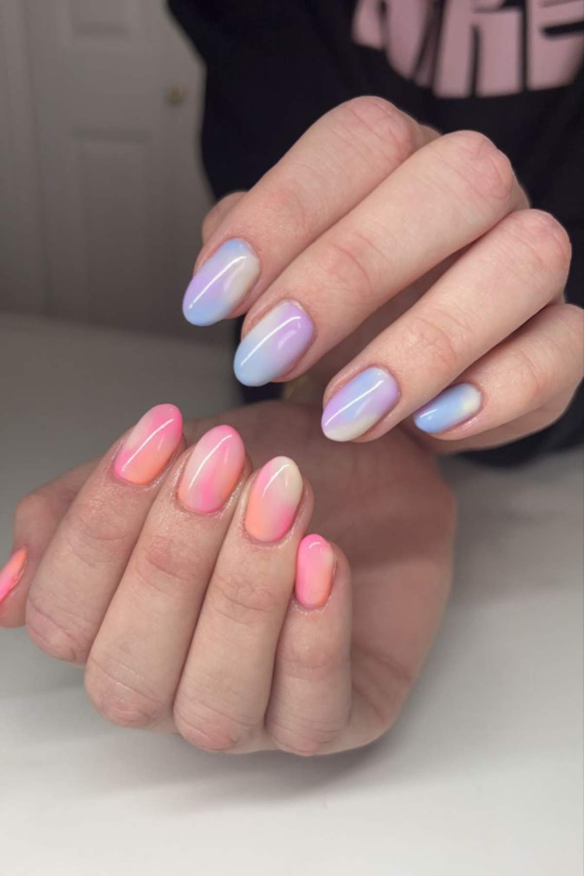 A person displays hands with almond-shaped nails, painted in a gradient of light blue to purple on one hand and pink to peach on the other.