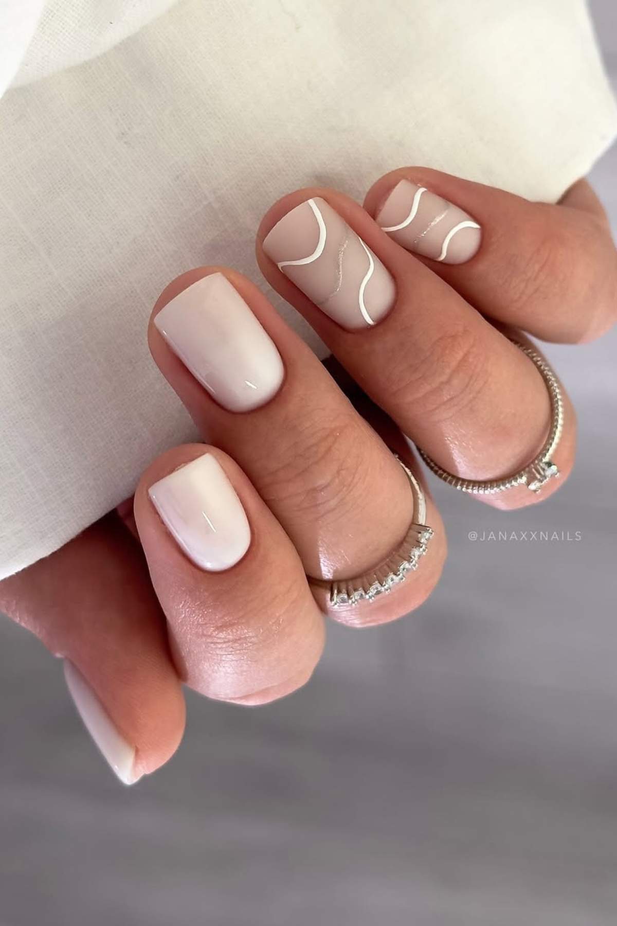 A hand with short, square-shaped nails painted in pale pink polish; two nails feature simple white wavy line designs.