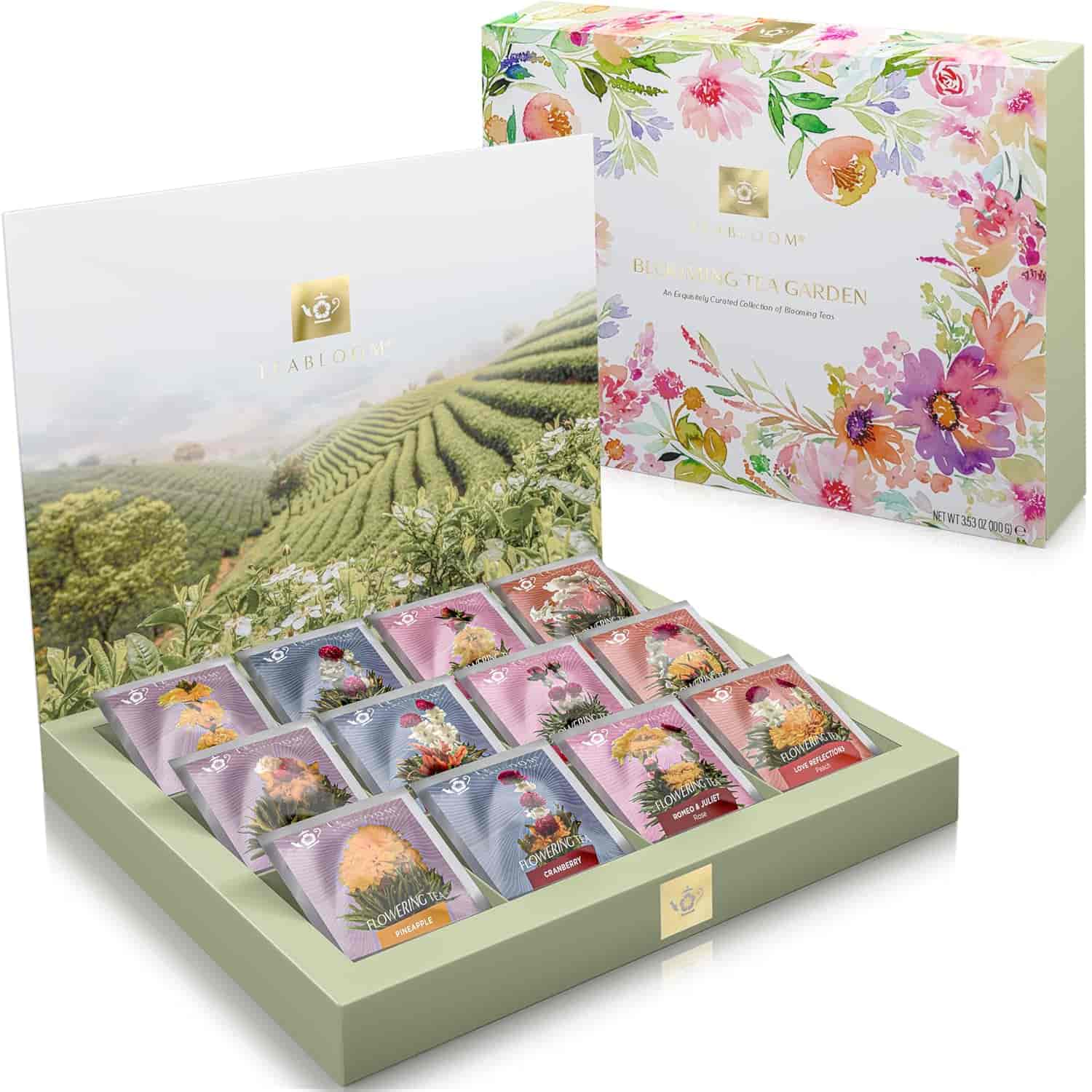 A decorative floral box containing assorted individually wrapped blooming tea bags, displayed upright with a scenic tea field backdrop inside the lid.