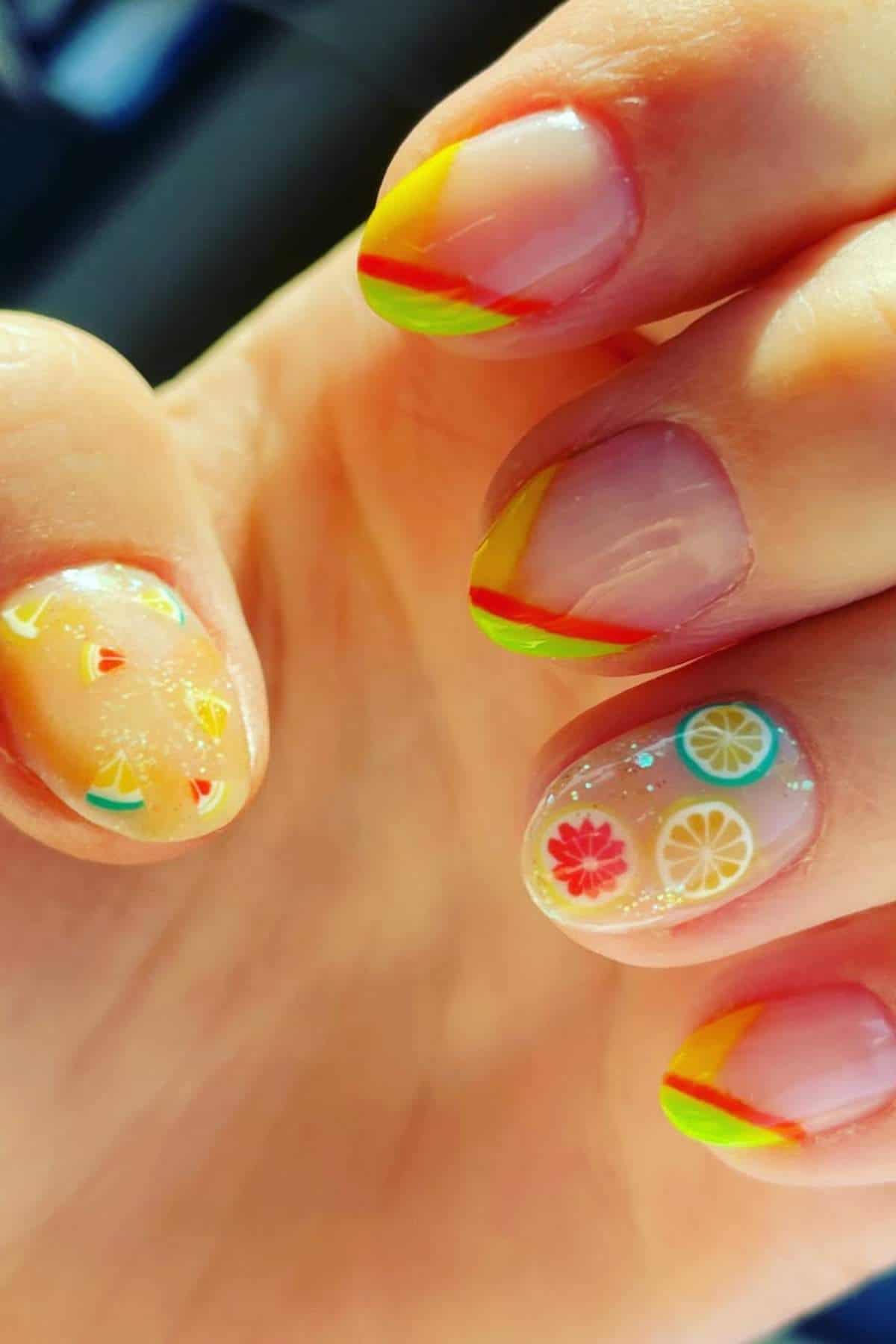 A hand with nails decorated with colorful fruit slice designs and bright, multicolored tips on a natural base.