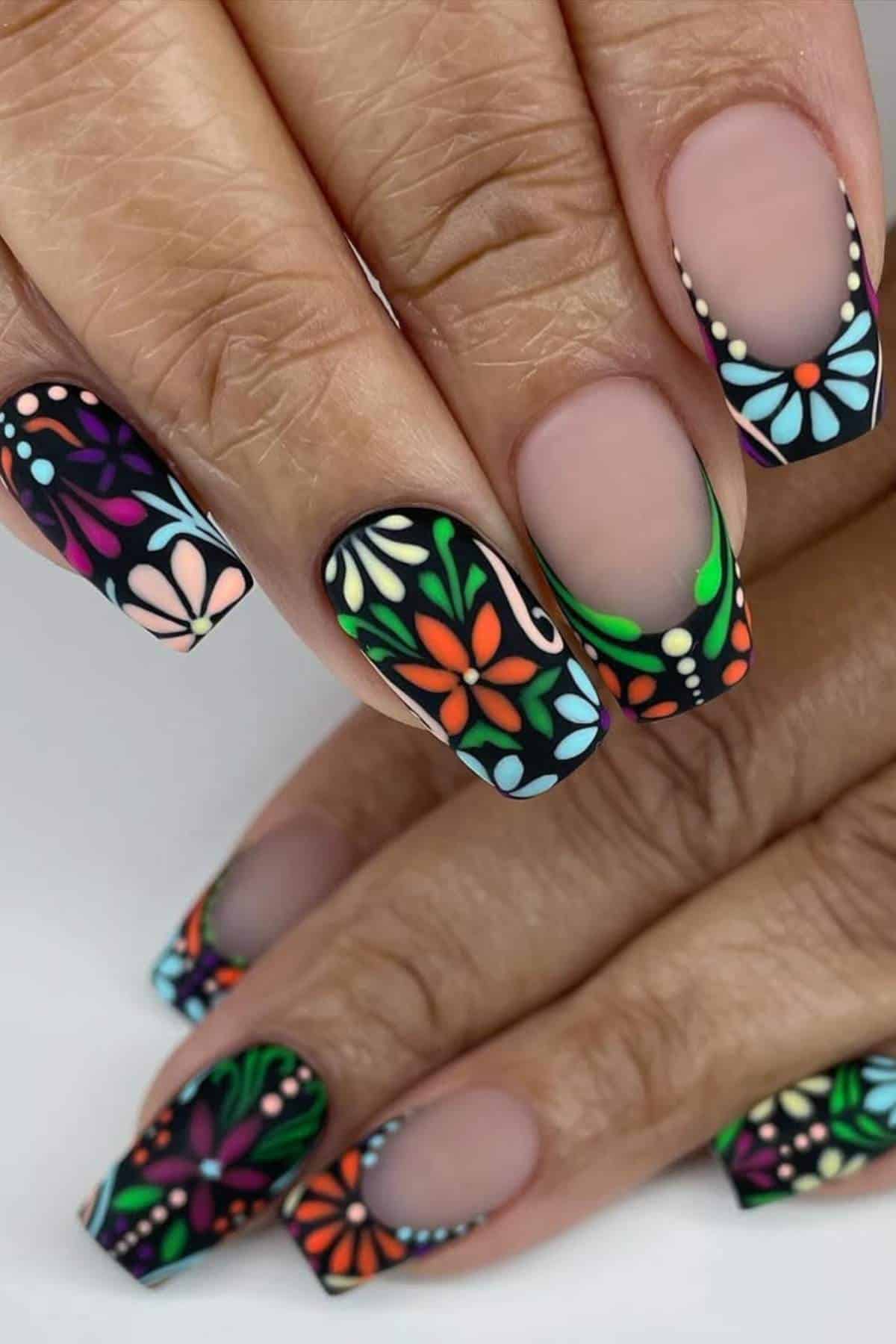 Close-up of hands with long nails featuring matte black backgrounds and colorful, intricate floral designs.