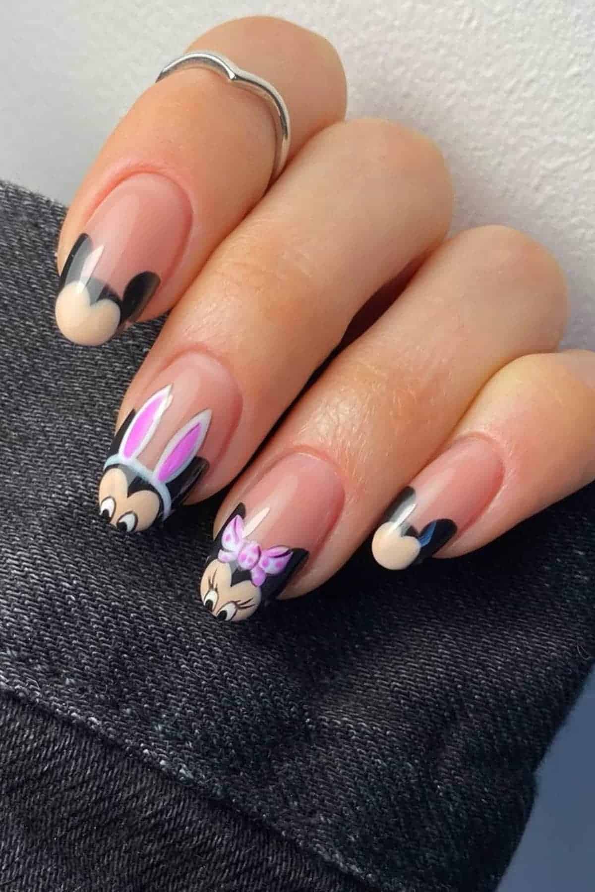A hand with long nails painted with Minnie Mouse-inspired nail art, featuring Minnie’s ears, pink bow, and bunny ears designs on a nude base.