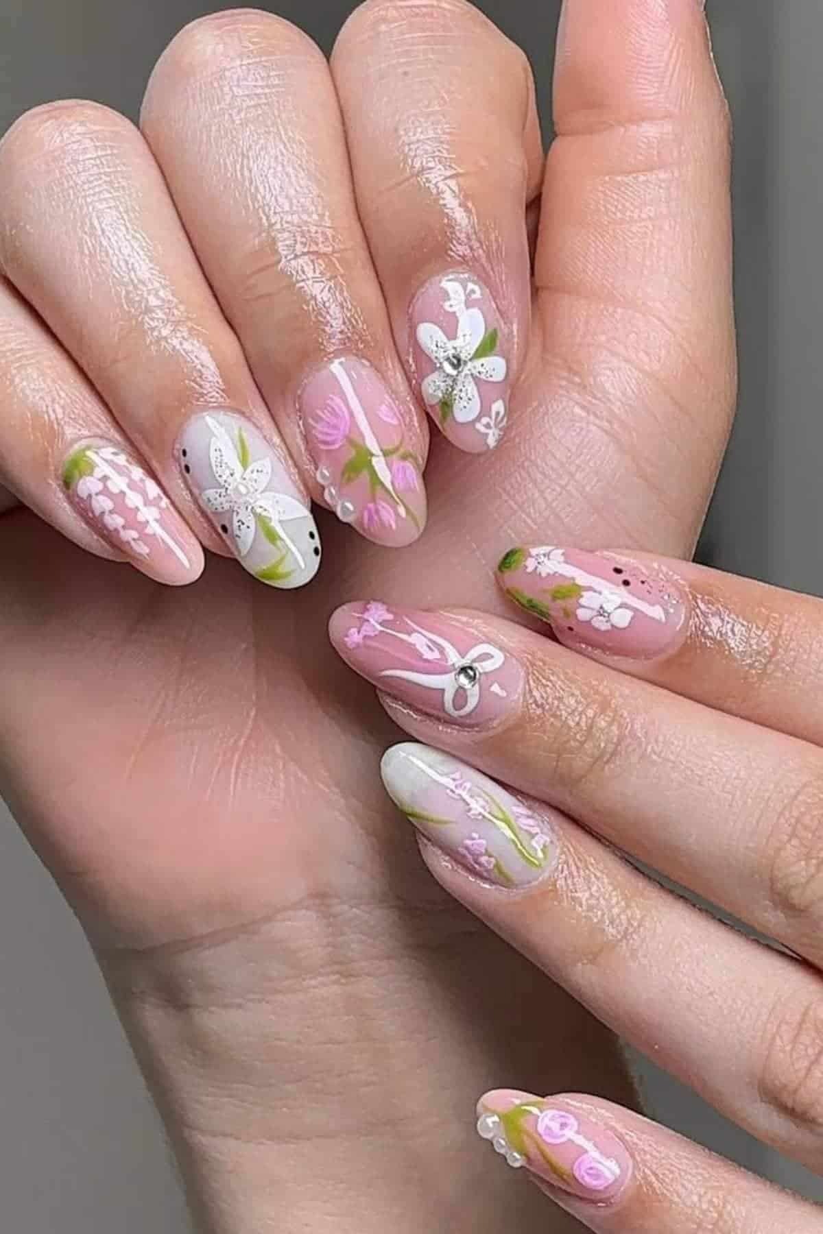 A hand with long, almond-shaped nails featuring intricate floral nail art in pastel pinks, whites, and greens.
