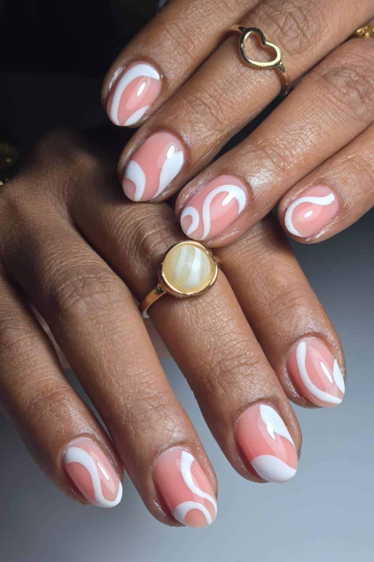 Hands with pink and white swirl nail art. The person is wearing a gold ring with a white stone and a gold heart-shaped ring.