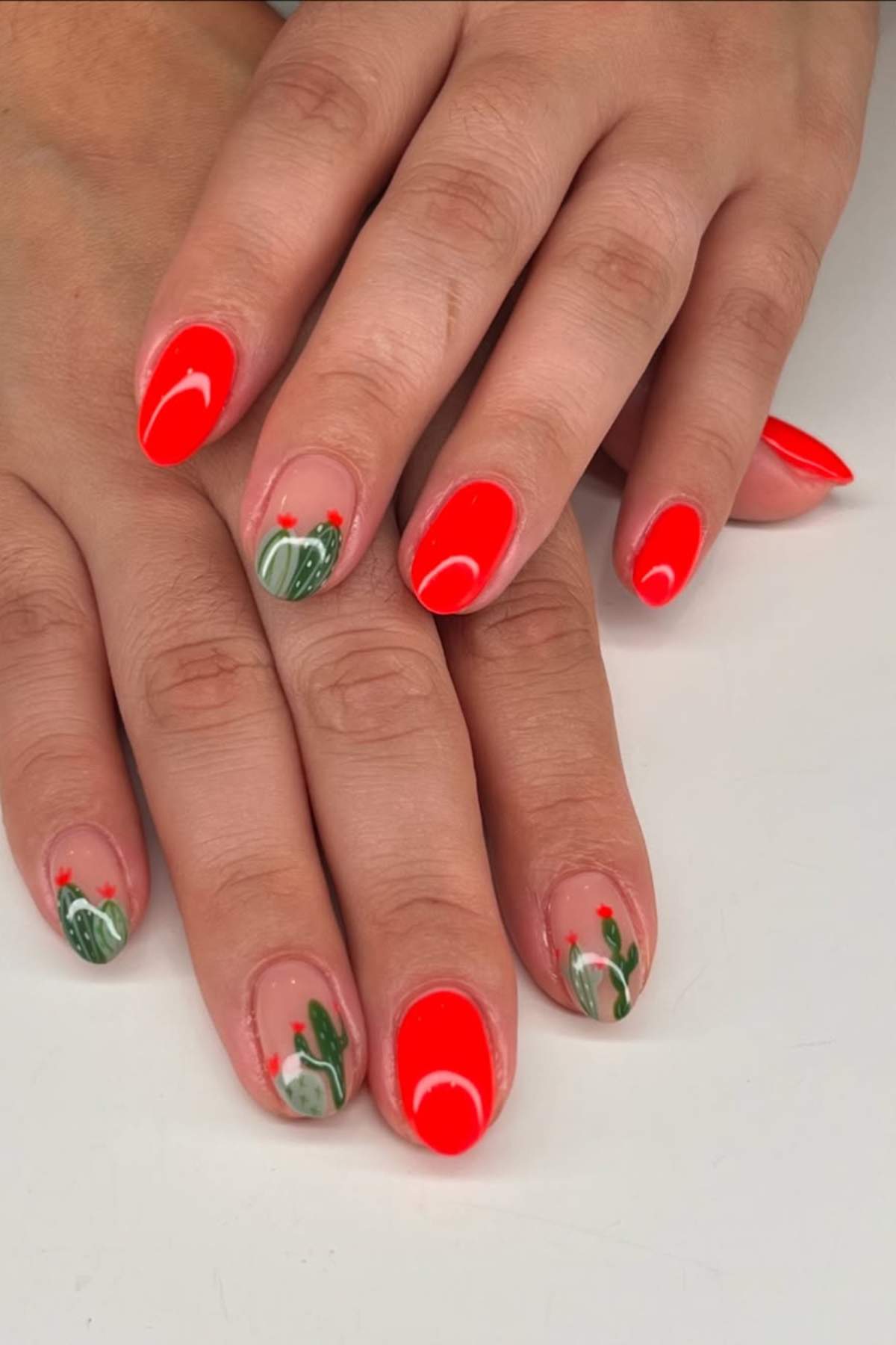 Hands with manicured nails; some nails are painted bright red, others have a cactus design on a nude base.