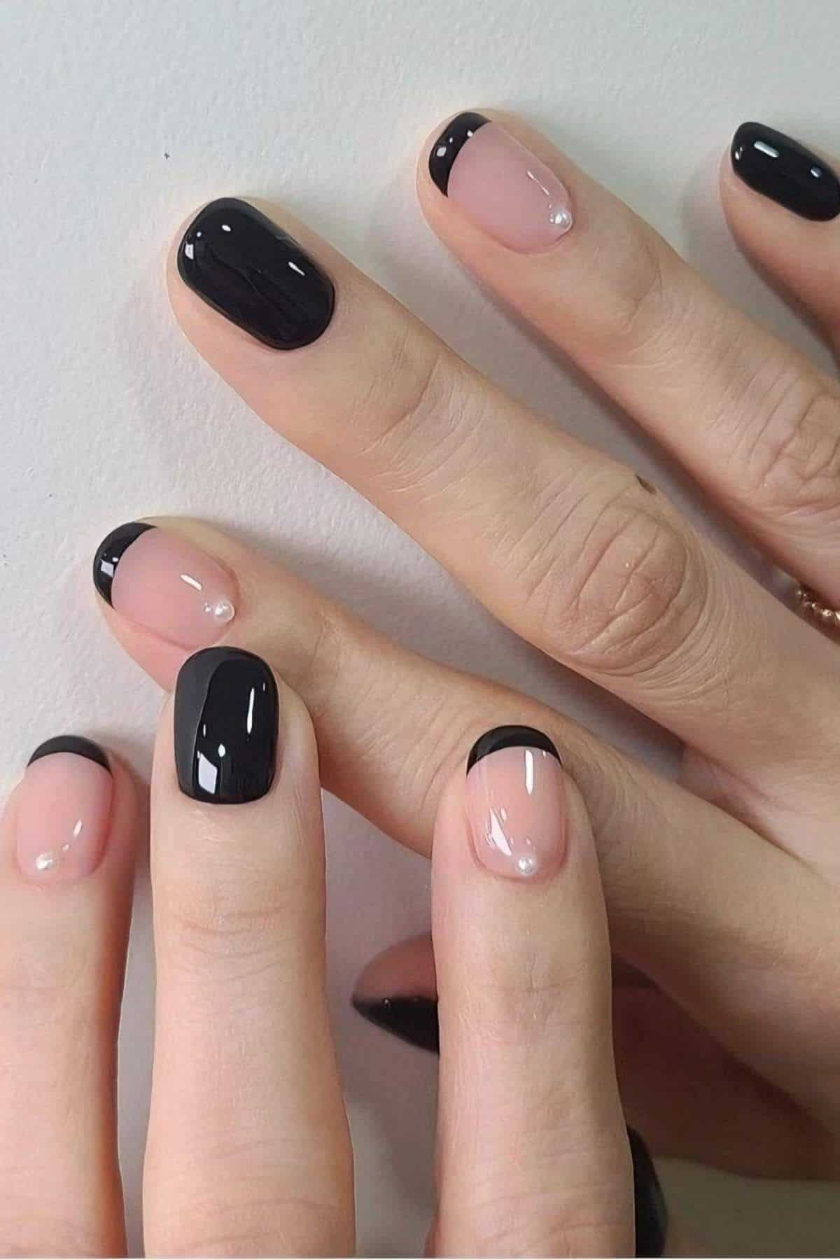 A close-up of hands with a manicure featuring nude nails with black French tips and some nails painted solid black.