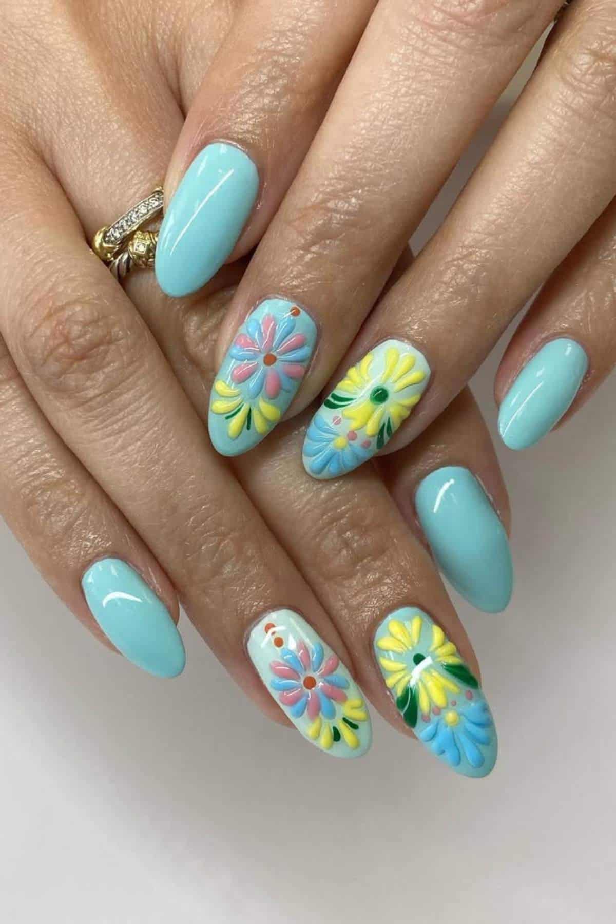 Hands with light blue manicured nails; three nails feature colorful, raised floral designs in pink, yellow, green, and blue.