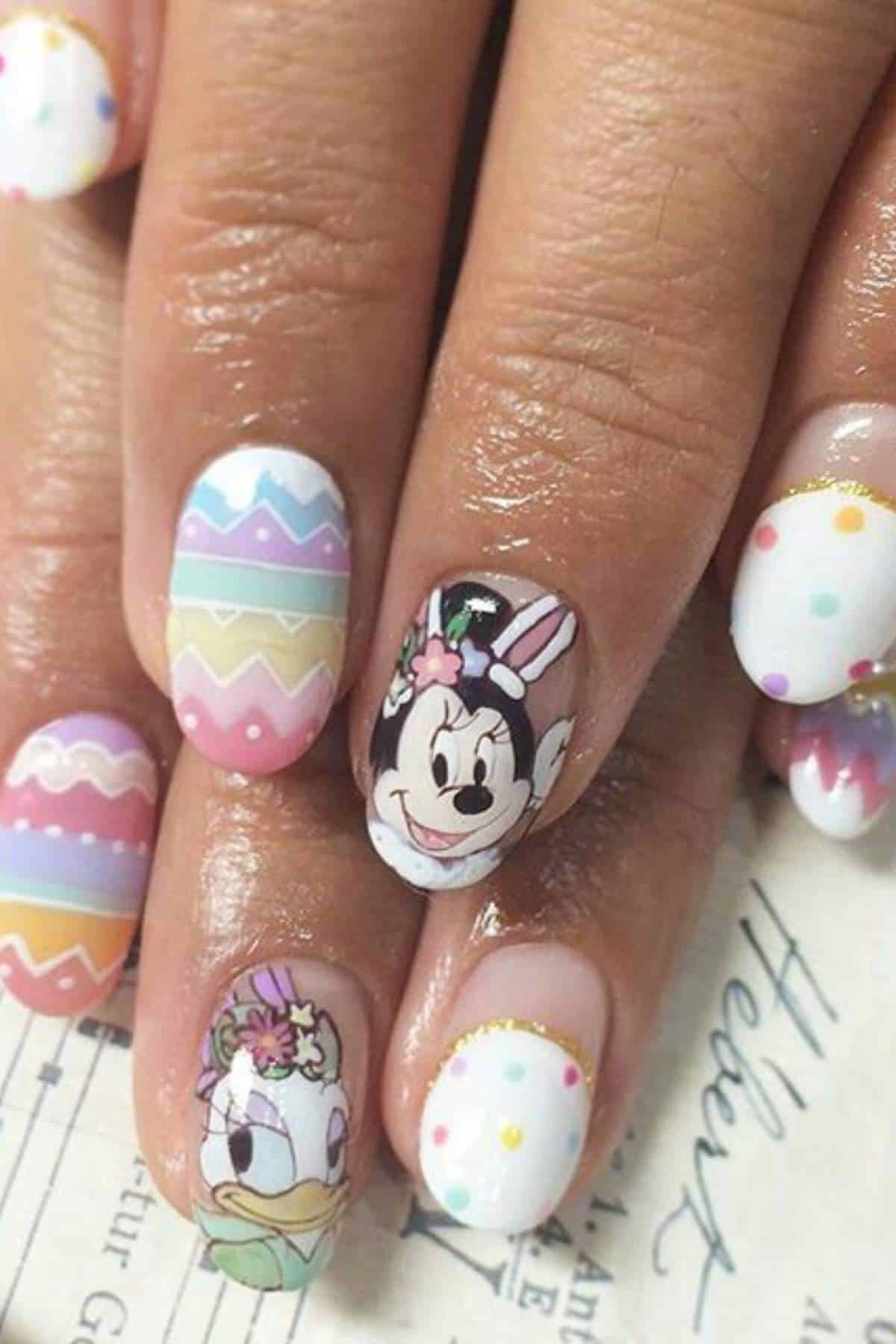 Close-up of nails with pastel Easter-themed designs, featuring cartoon characters Minnie Mouse and Daisy Duck, colorful patterns, and polka dots.