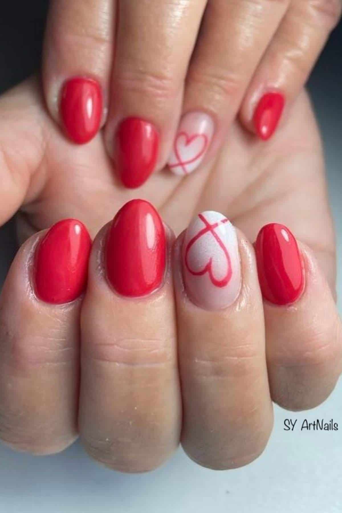 A hand with red oval-shaped nails; one nail features a light pink base with a red outline heart design.