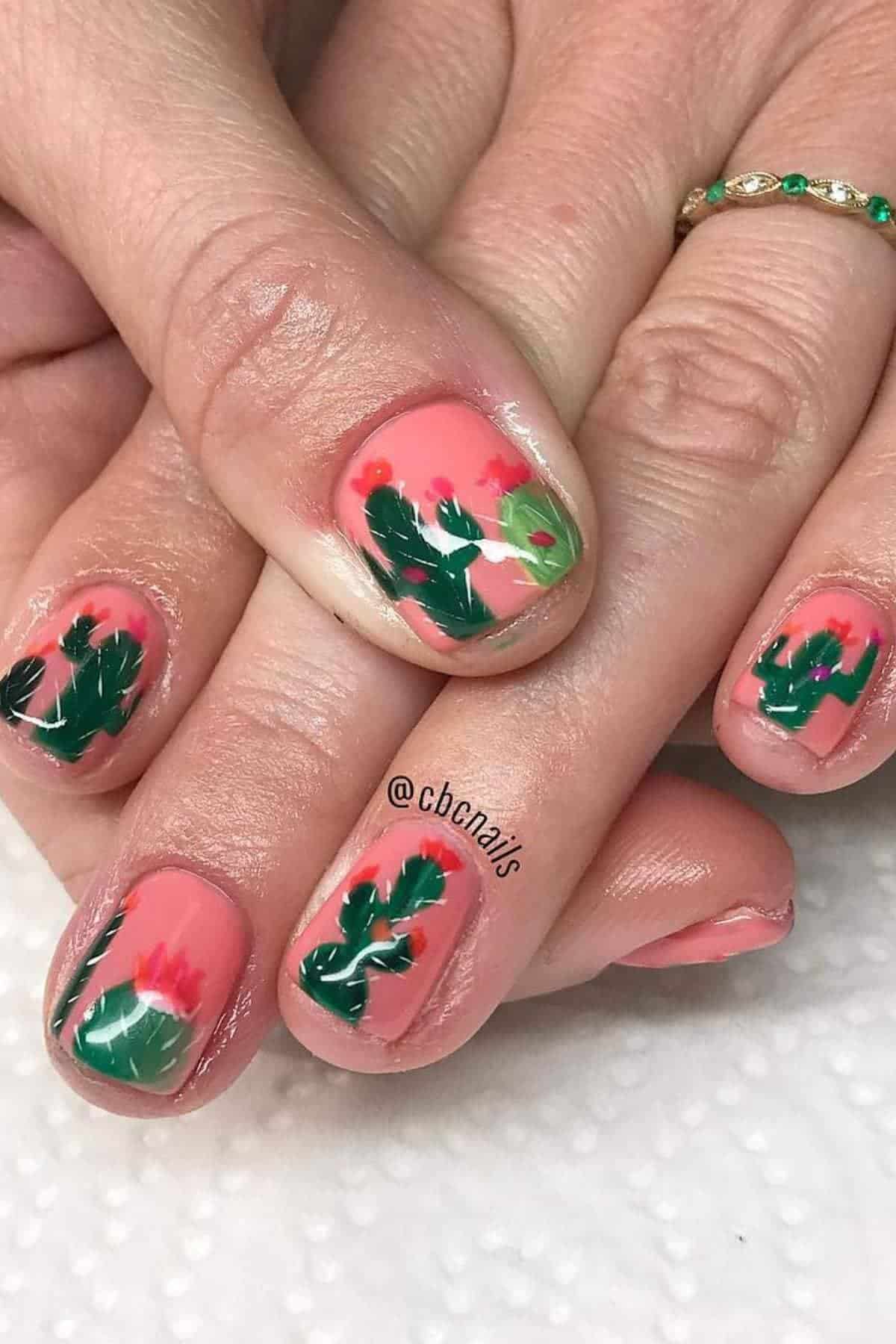 Close-up of hands with short nails painted with a pink base and green leaves with red flower nail art.