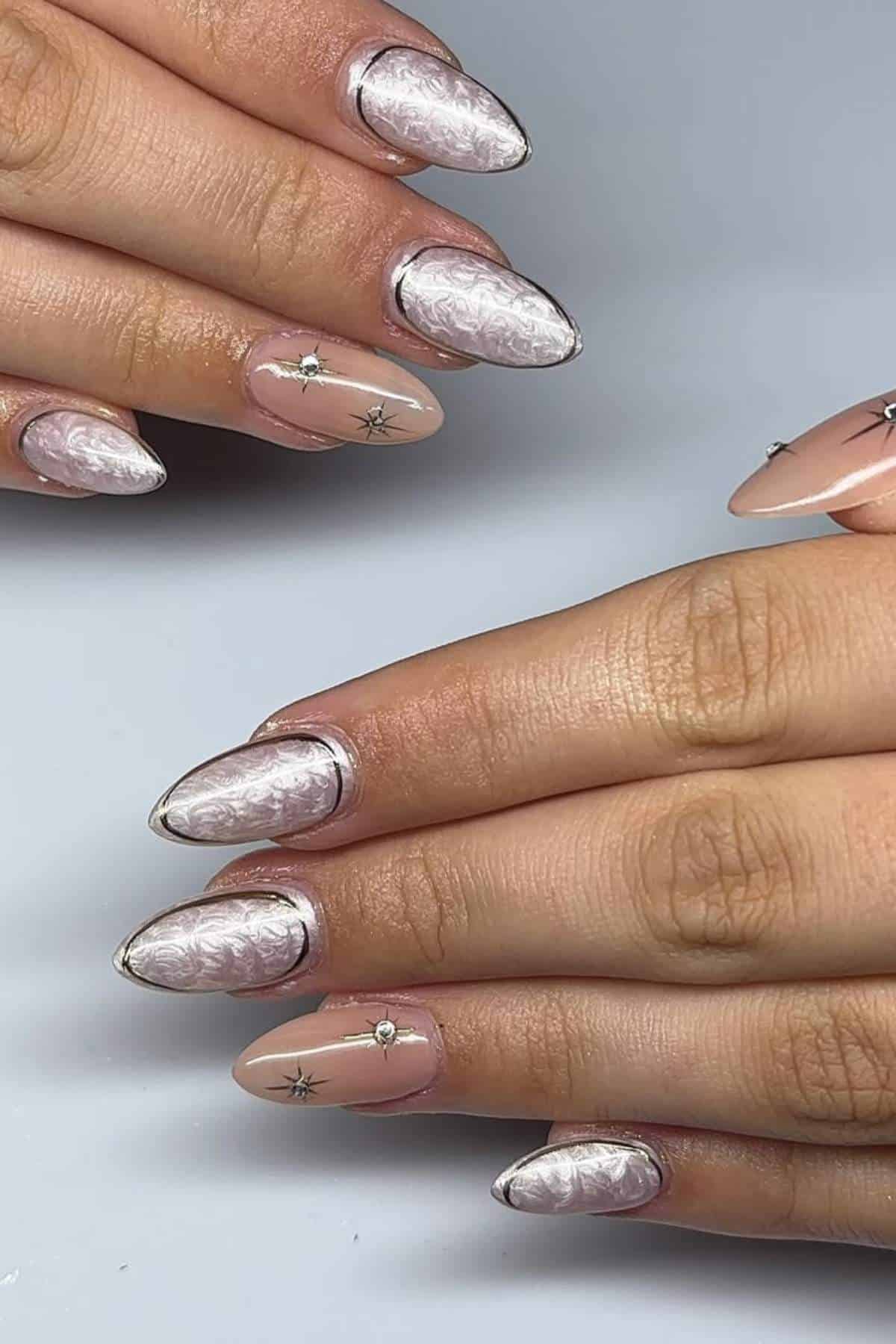 Close-up of hands with almond-shaped nails featuring a pearlescent white design, silver metallic tips, and small rhinestone accents on a pale pink base.