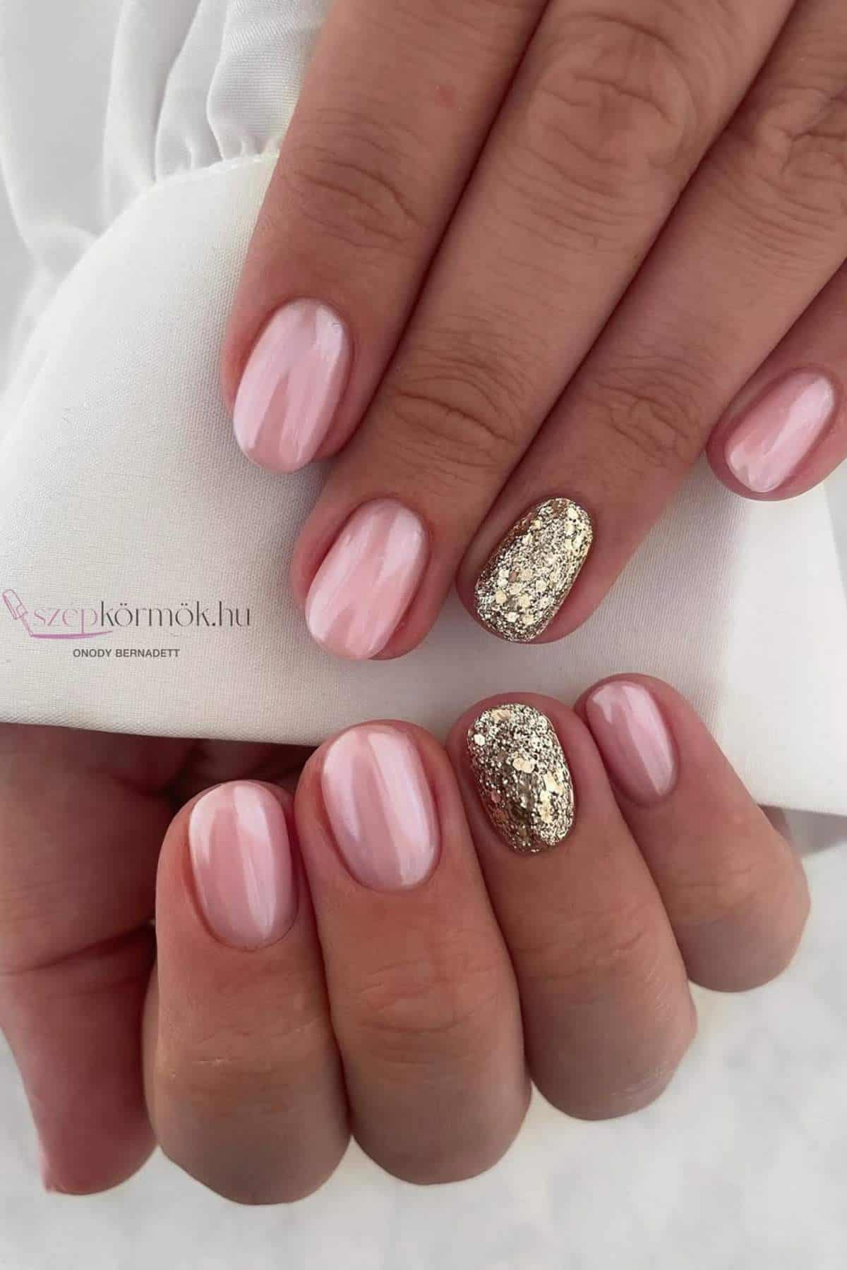 Hands with short nails painted light pink; ring fingernails feature glittery gold polish.