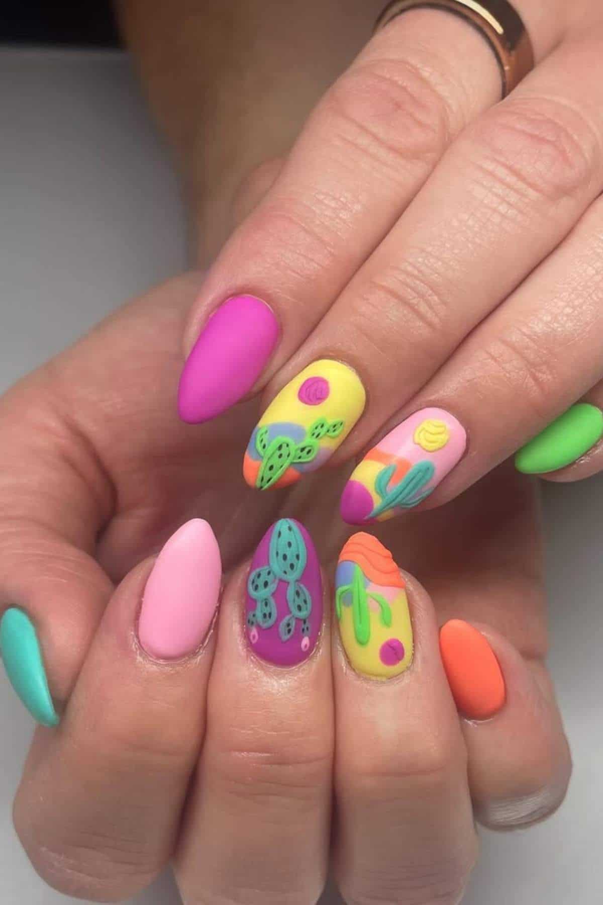 Hands with long, almond-shaped nails painted in bright matte colors, featuring cactus and abstract designs on some nails.