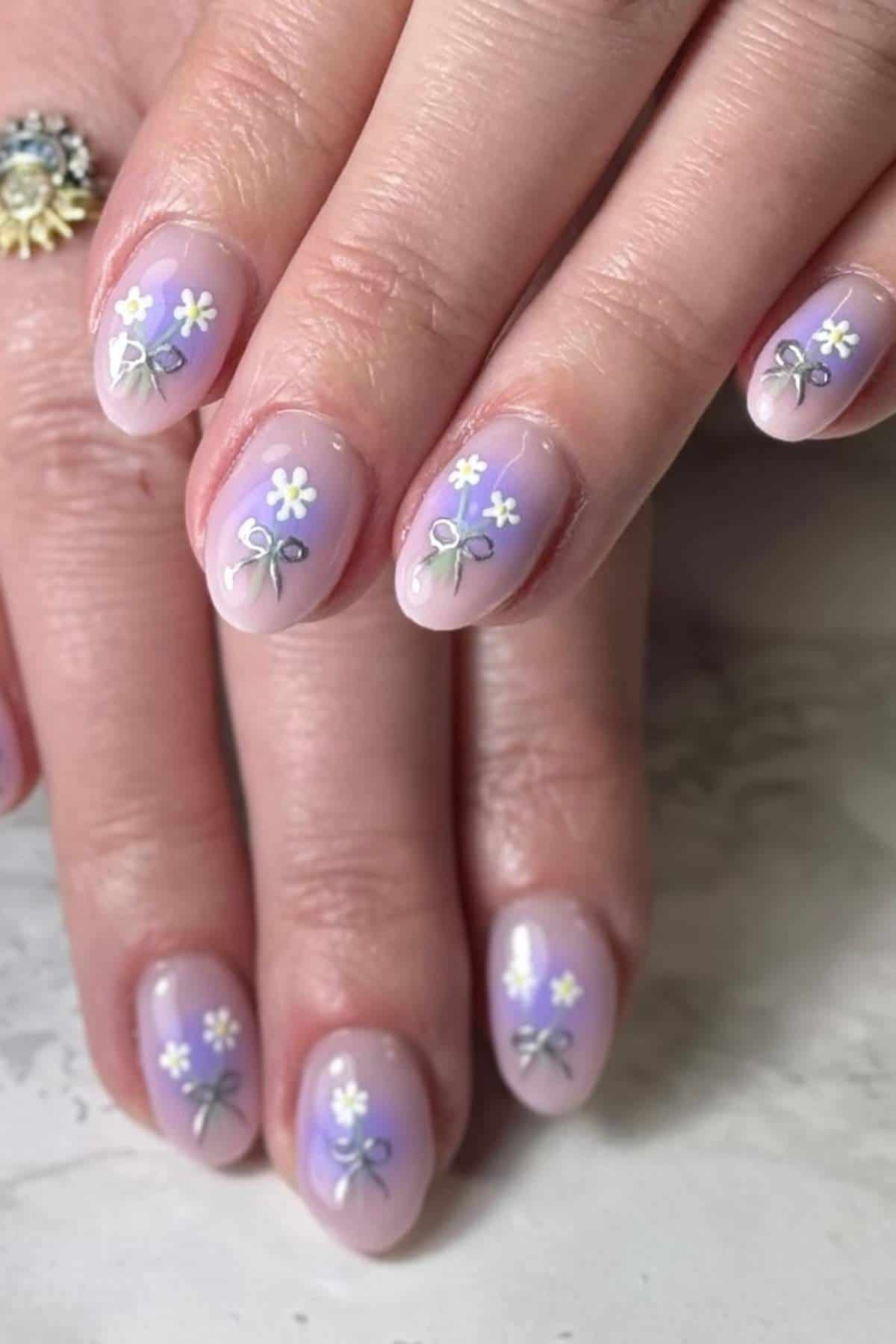 Close-up of hands with light purple manicure featuring small white flowers and silver bow designs on each nail.