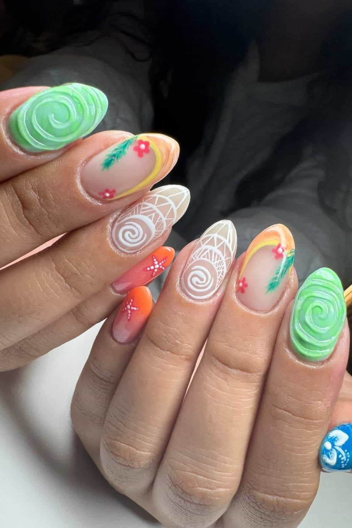 Close-up of hands with long, colorful acrylic nails featuring swirls, floral designs, geometric patterns, and a variety of bright colors including green, orange, yellow, and blue.