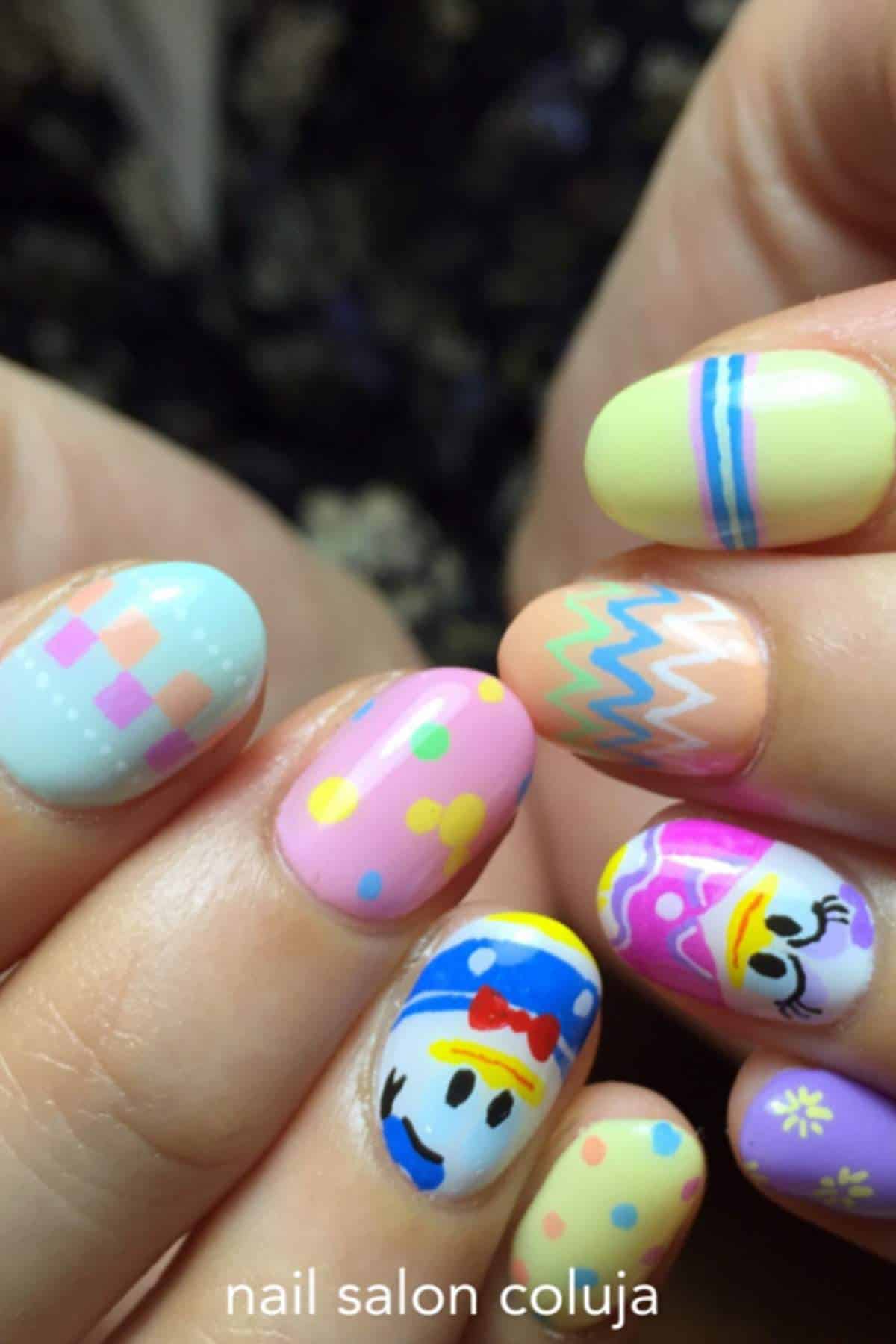 Close-up of hands with colorful, Easter-themed nail art featuring patterns, polka dots, and cartoon characters on short, rounded nails.