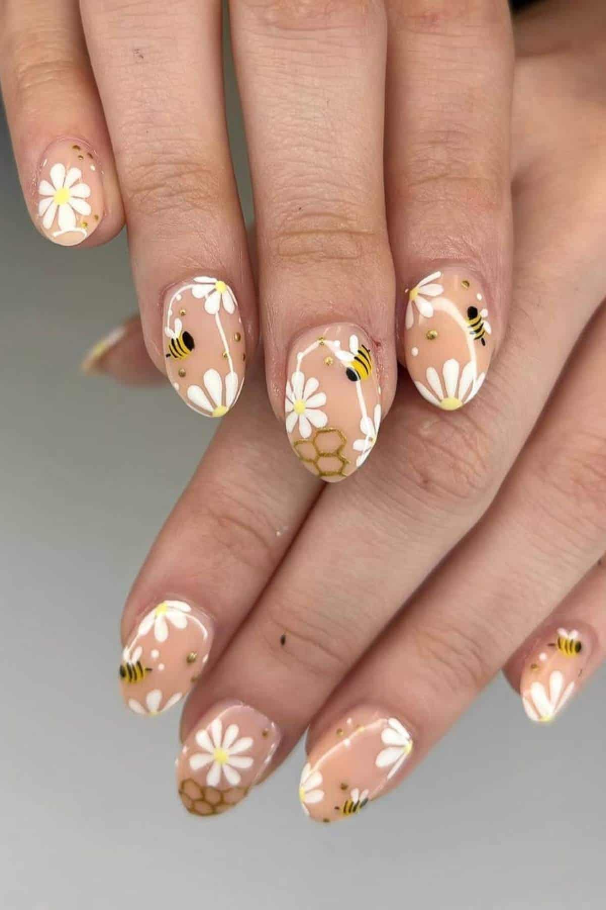 Hands with almond-shaped nails featuring daisy flowers, bees, honeycomb patterns, and nude polish.