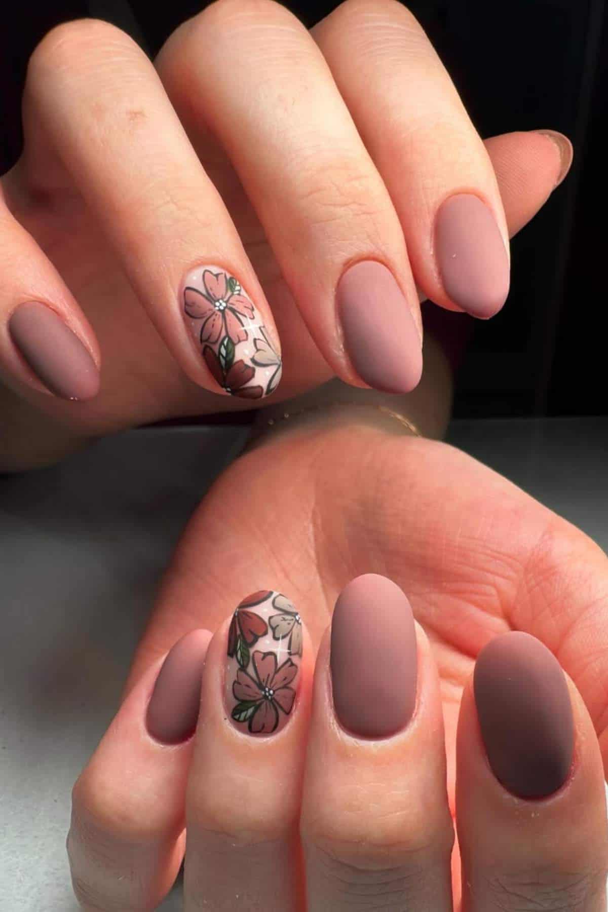 Hands with matte mauve almond-shaped nails; one accent nail on each hand features a floral design with pink, white, and green flowers.