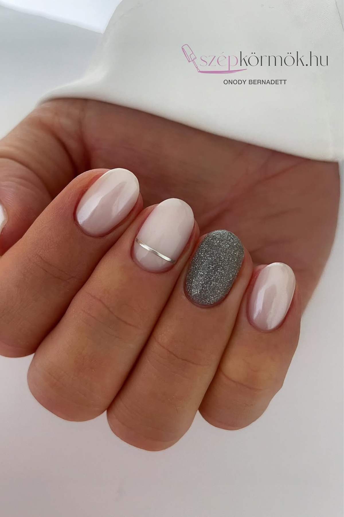 A hand with manicured nails featuring light pink polish, one accent nail with silver glitter, and one nail with a thin silver stripe.
