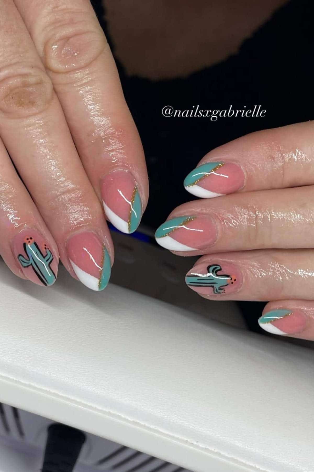 A close-up of manicured hands with almond-shaped nails featuring white and green tips, gold accents, and cactus designs on two nails.