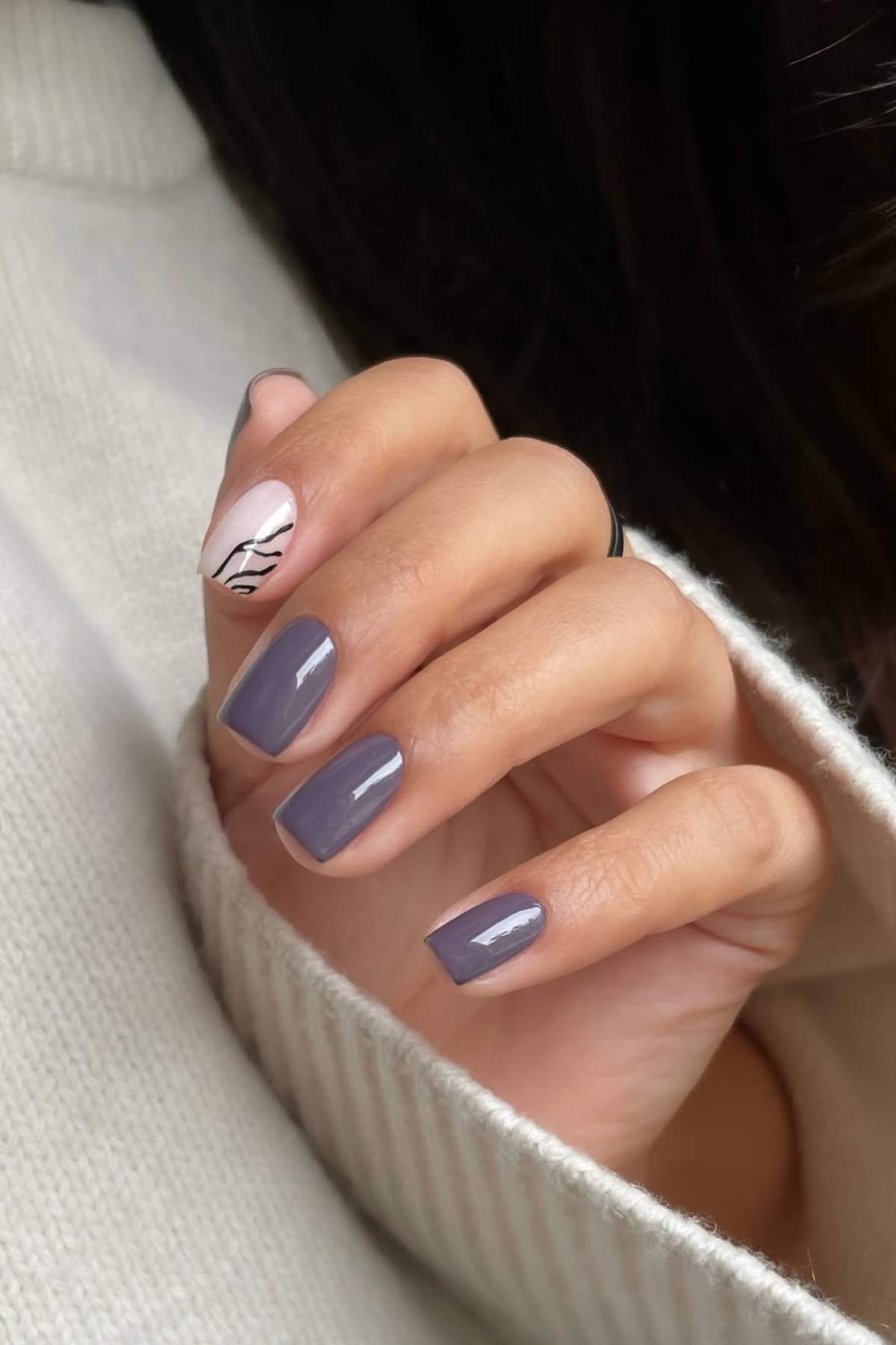 A hand with short, square-shaped nails painted purple, except for the index finger which is painted light pink with a black line art design.