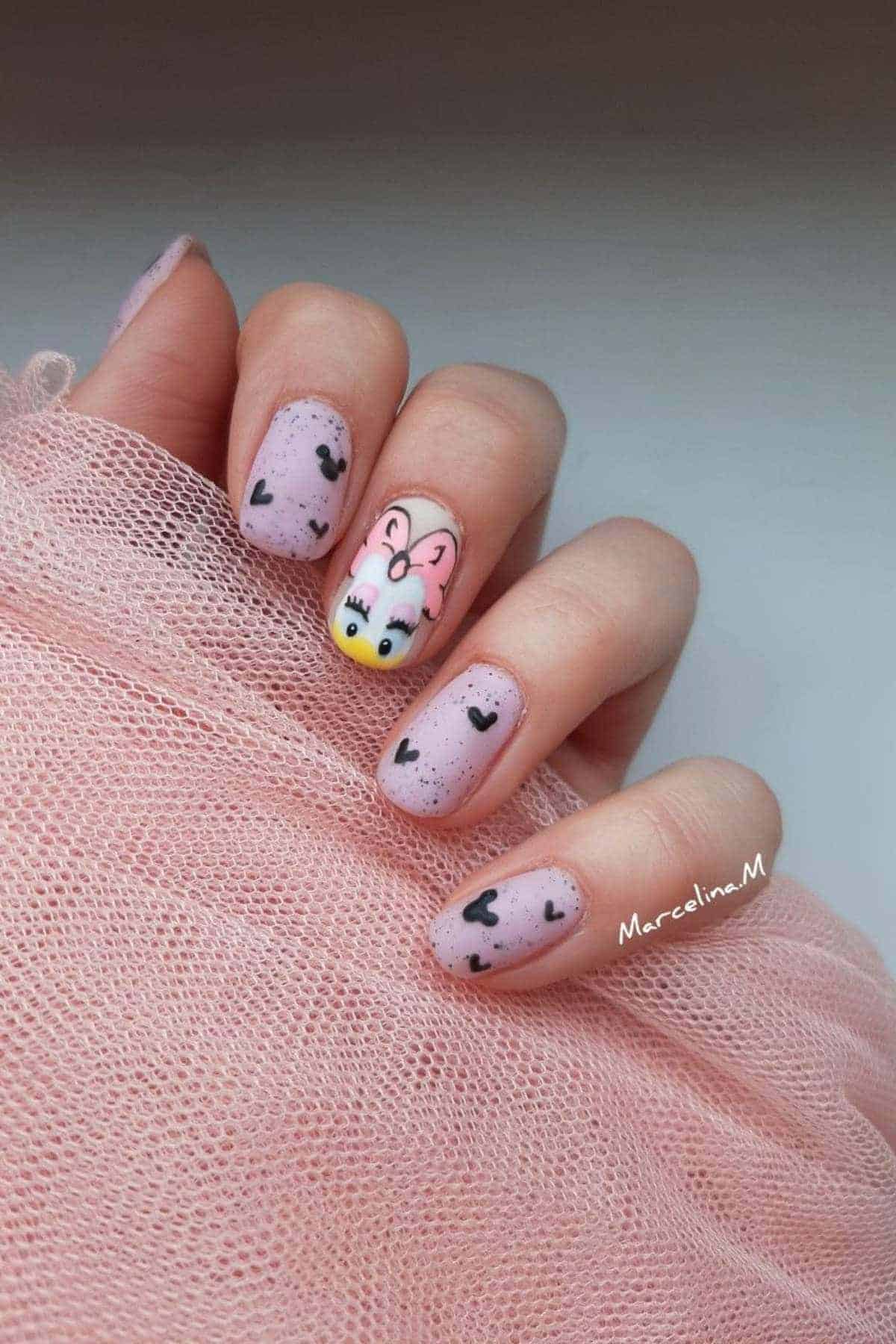 A hand with light pink nail polish featuring black hearts and one accent nail with a cartoon duck with a pink bow.
