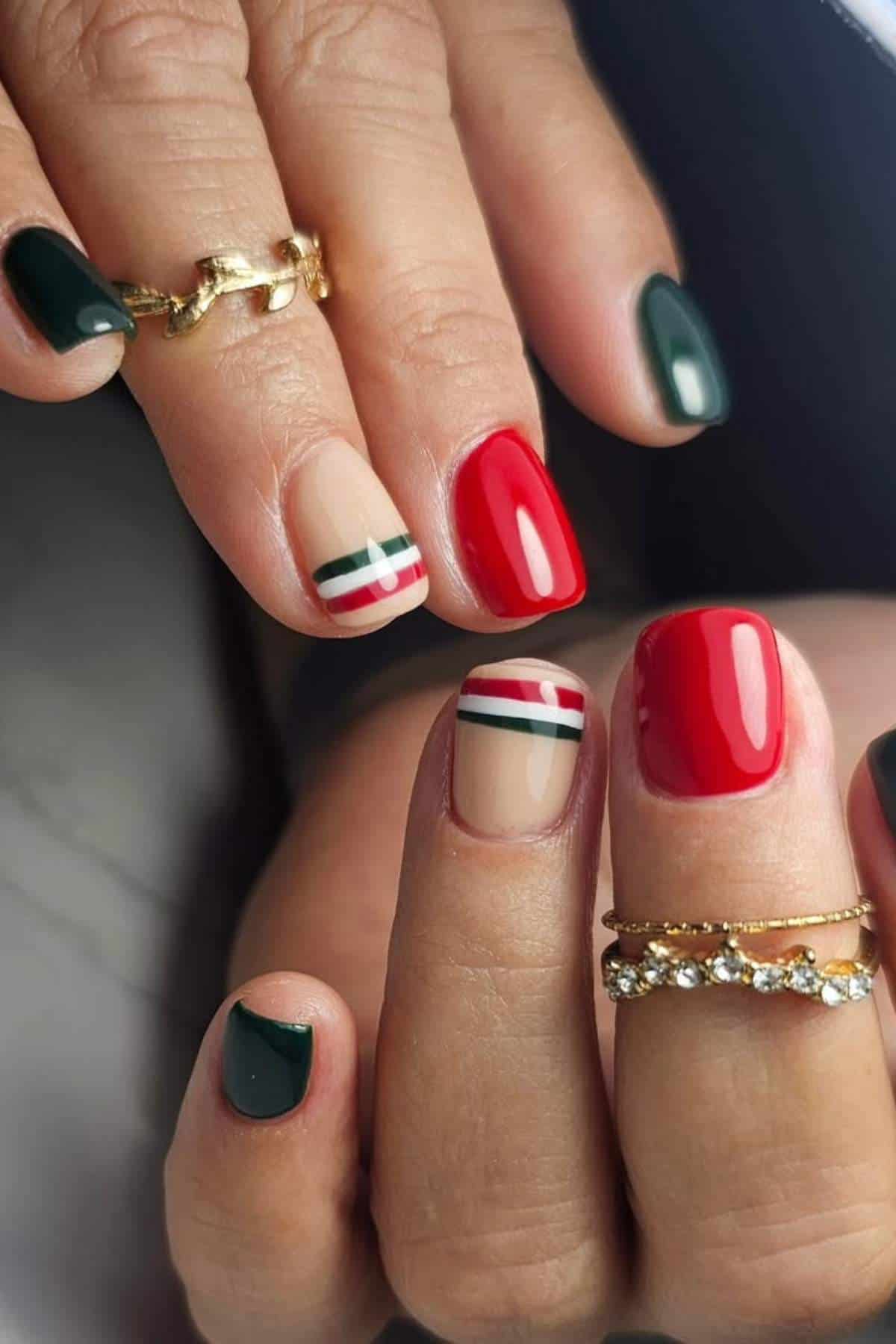 Close-up of hands with manicured nails in dark green, red, and nude colors, some with red and green stripes; gold rings adorn the fingers.
