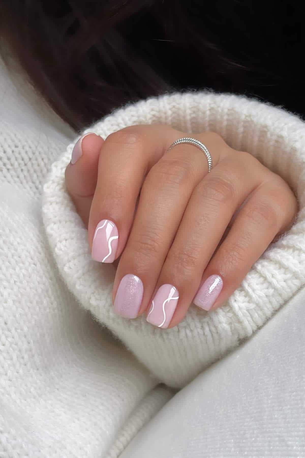 A hand with light pink manicured nails featuring white abstract lines, resting on a white sweater.