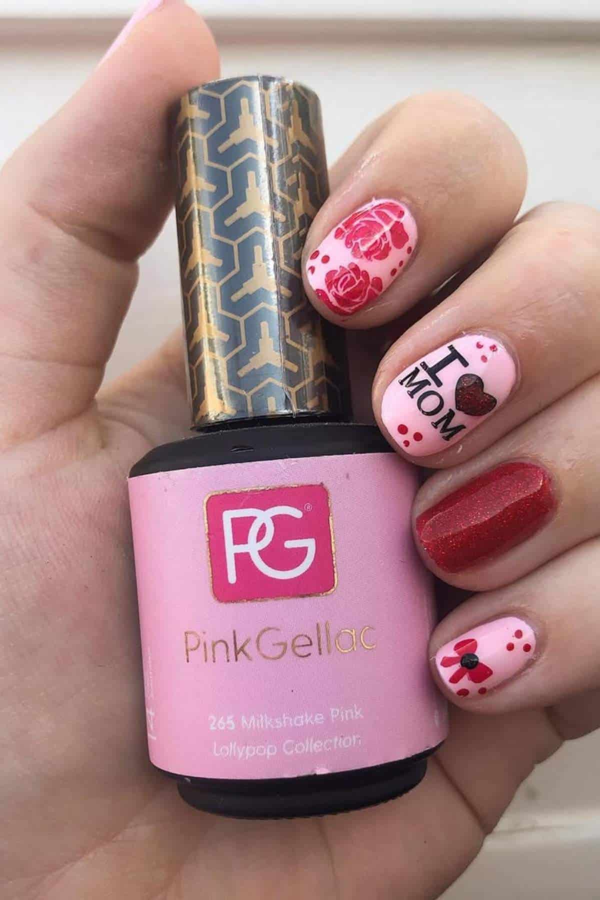 A hand with nail art holds a bottle of Pink Gellac nail polish. Nails are painted pink and red with rose, heart, and "I ♥ MOM" designs.