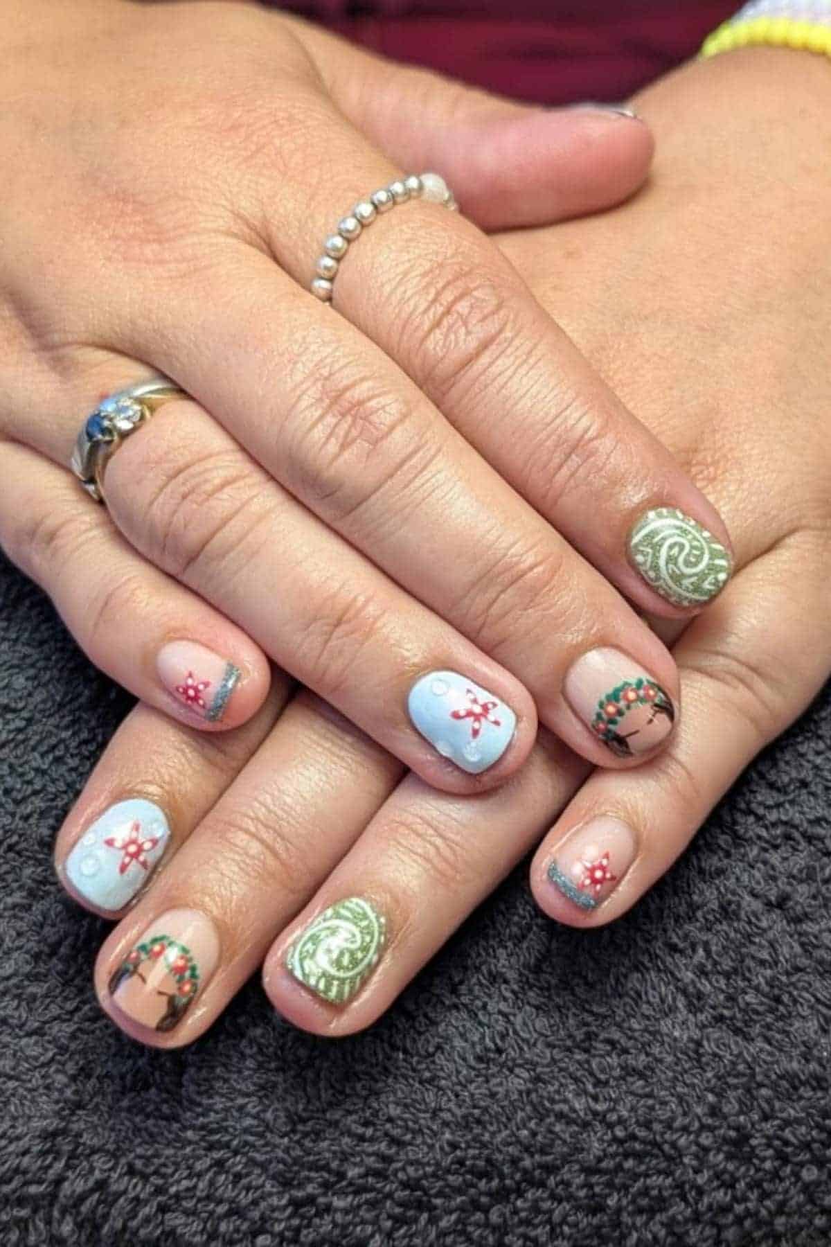 Hands with festive nail art featuring gingerbread men, wreaths, candy canes, snowflakes, and green swirls on short, rounded nails.