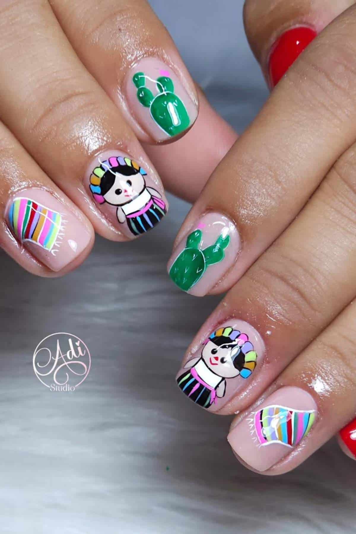 Close-up of hands with nail art featuring colorful Mexican doll faces, green cacti, striped patterns, and one red-painted nail.