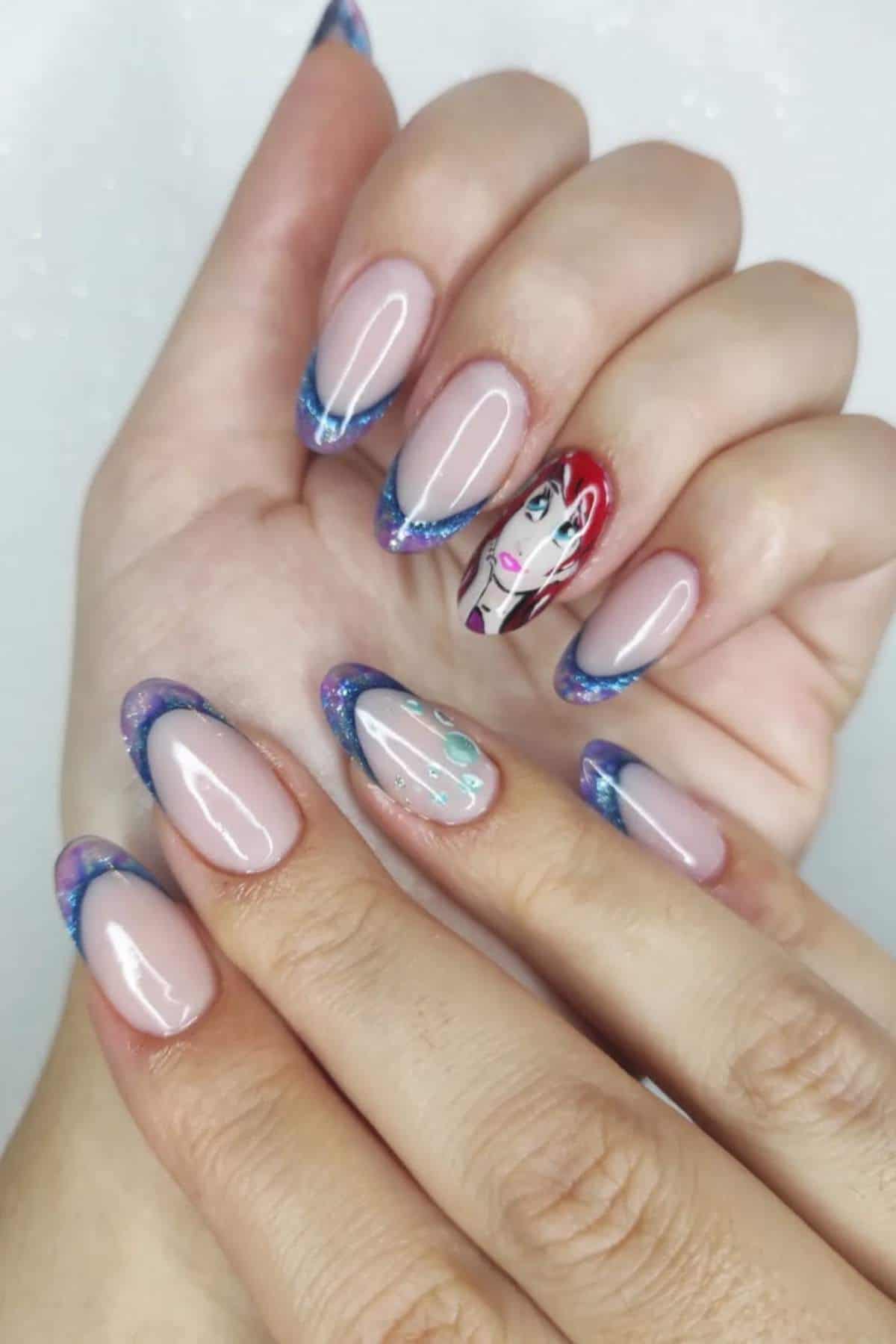 A hand with almond-shaped nails featuring blue and purple French tips, with one accent nail displaying a painted face with red hair and colorful details.