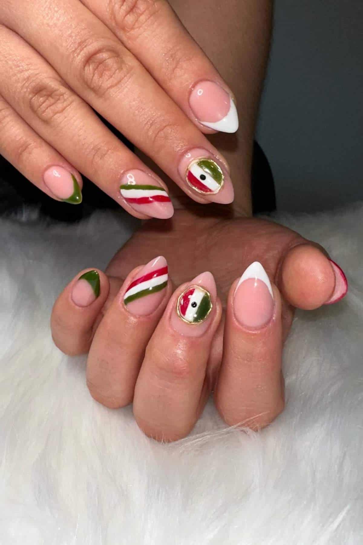 A hand with almond-shaped nails featuring French tips and accent nails decorated with red, green, and white striped and abstract designs, resting on a white fur surface.