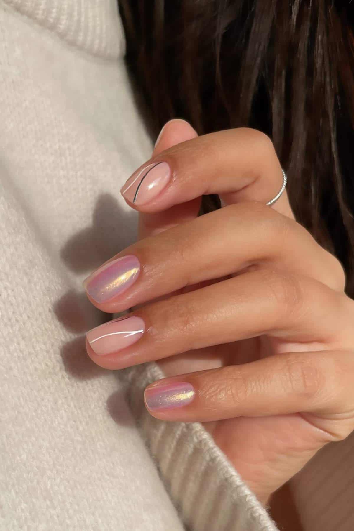 A hand with short, iridescent pink nails and a fine black line design on one nail, shown against a white sweater.
