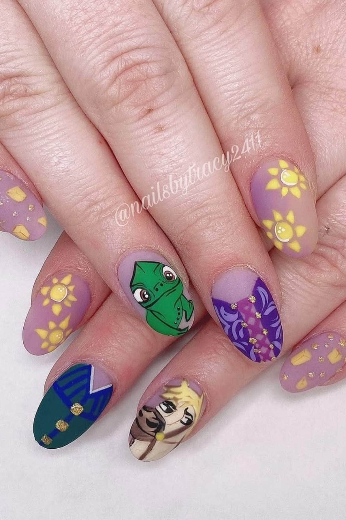 A set of manicured nails with Tangled-themed nail art, including Rapunzel, Pascal the chameleon, sun motifs, and purple and green designs.