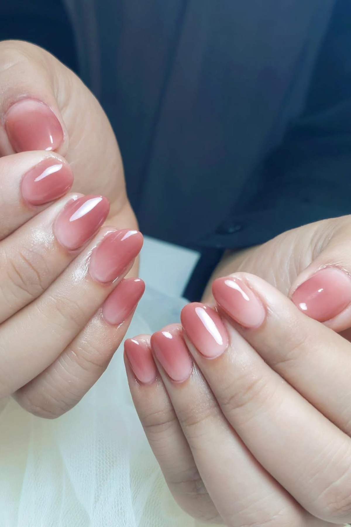Close-up of hands with short, oval-shaped nails painted in a glossy, natural pink shade.