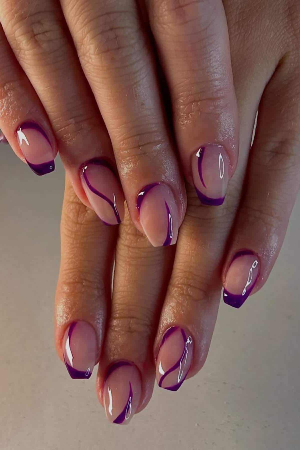 Close-up of hands with short nails featuring a nude base and abstract purple lines and tips, displayed against a plain background.