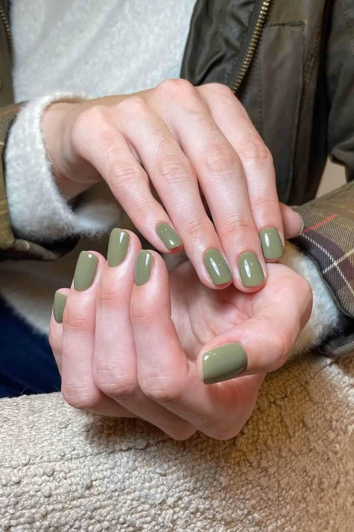 Close-up of hands with short, neatly manicured nails painted in a glossy olive green shade.