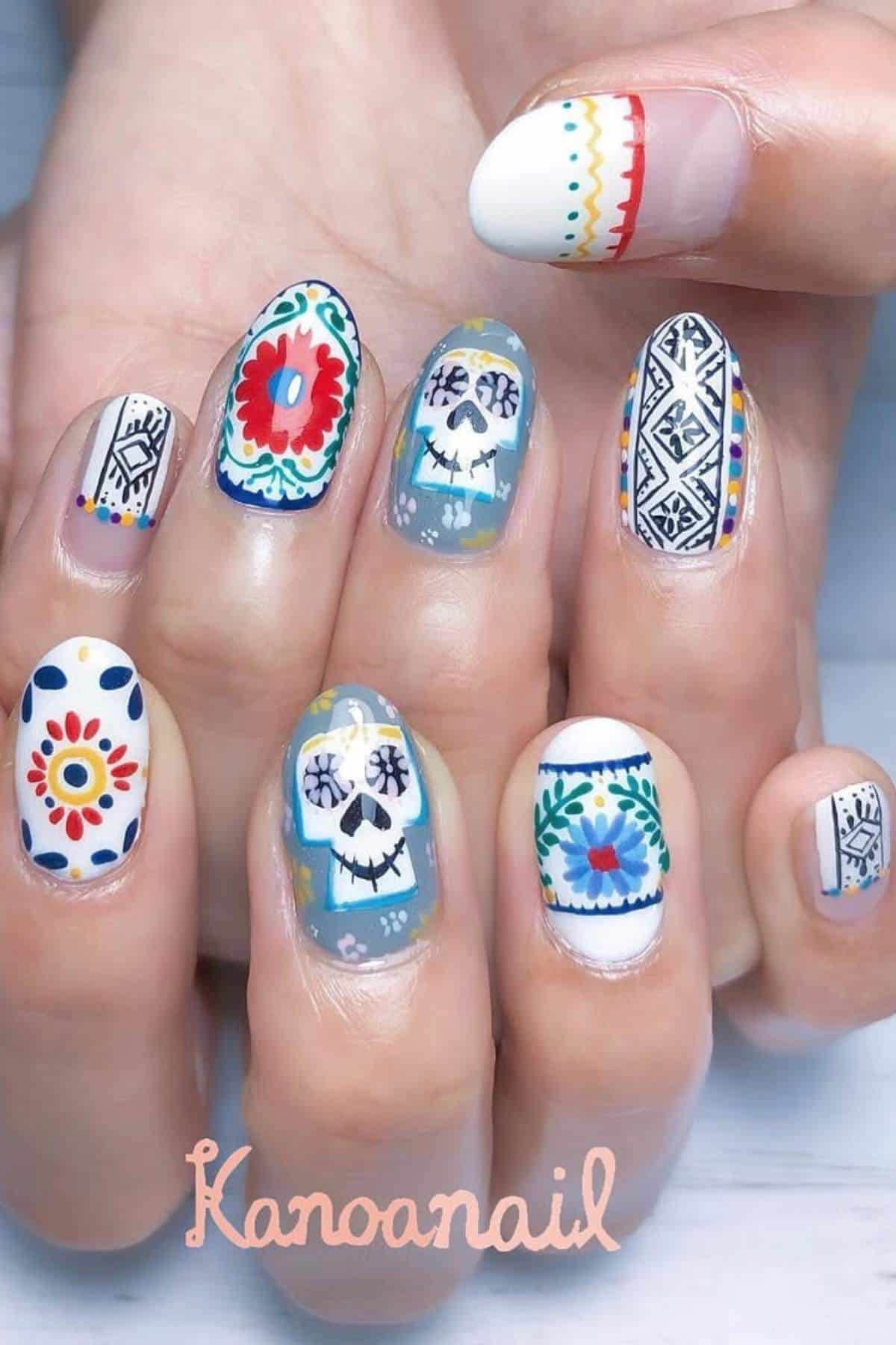 A hand with colorful nail art featuring floral patterns, geometric designs, and sugar skull motifs on each fingernail.